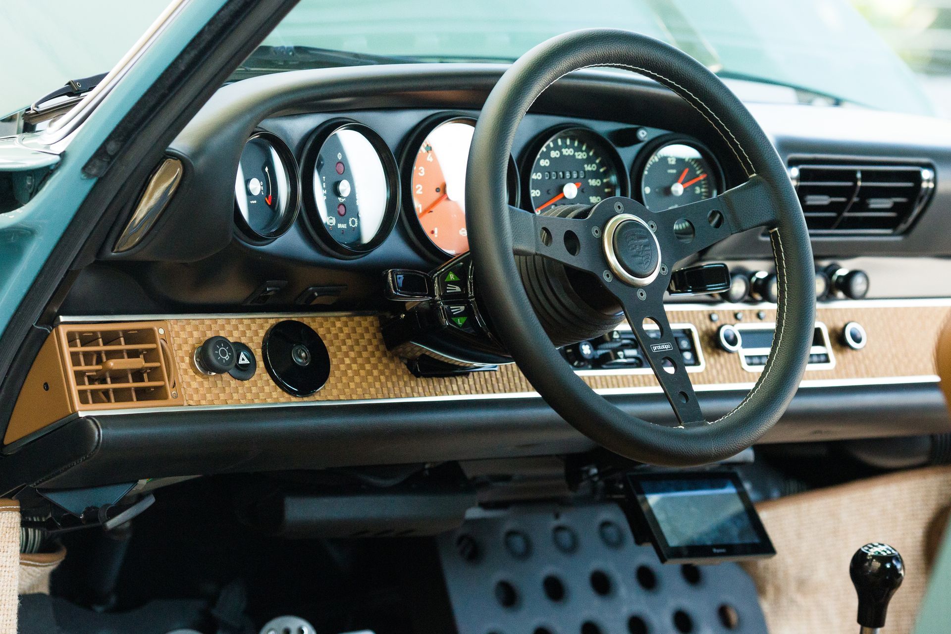 Dashboard of a classic car with black steering wheel, gauges, and a gold-colored dashboard.