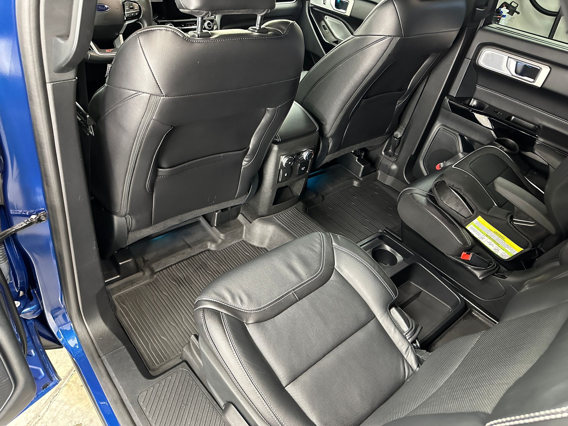 Interior view of a blue car's rear seats with black leather upholstery, including a child car seat.
