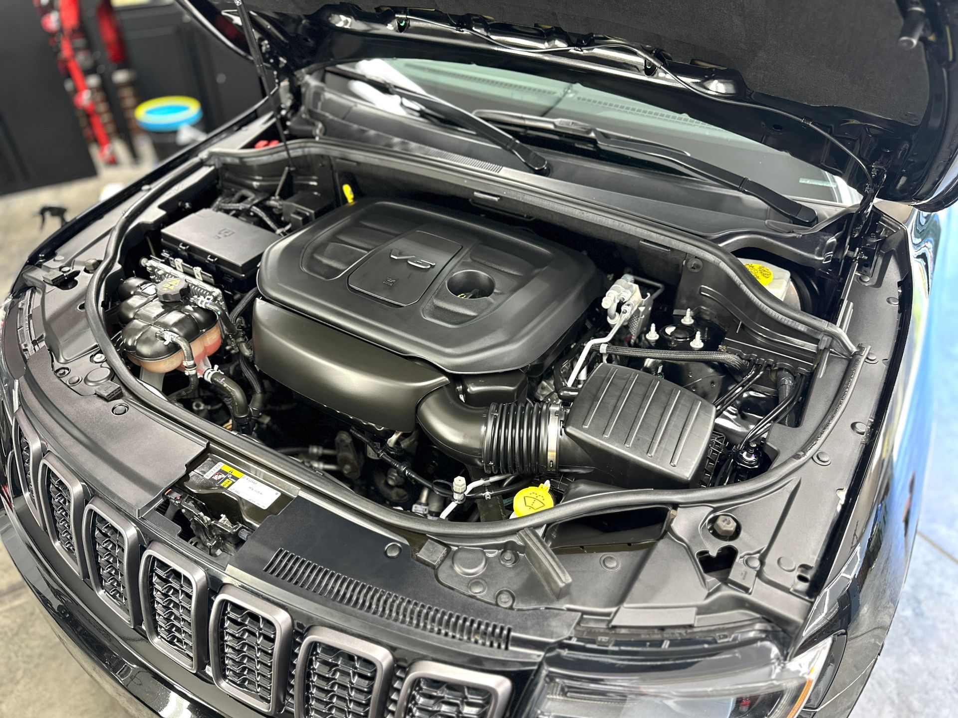 Black Jeep engine compartment, hood open, detailing work.