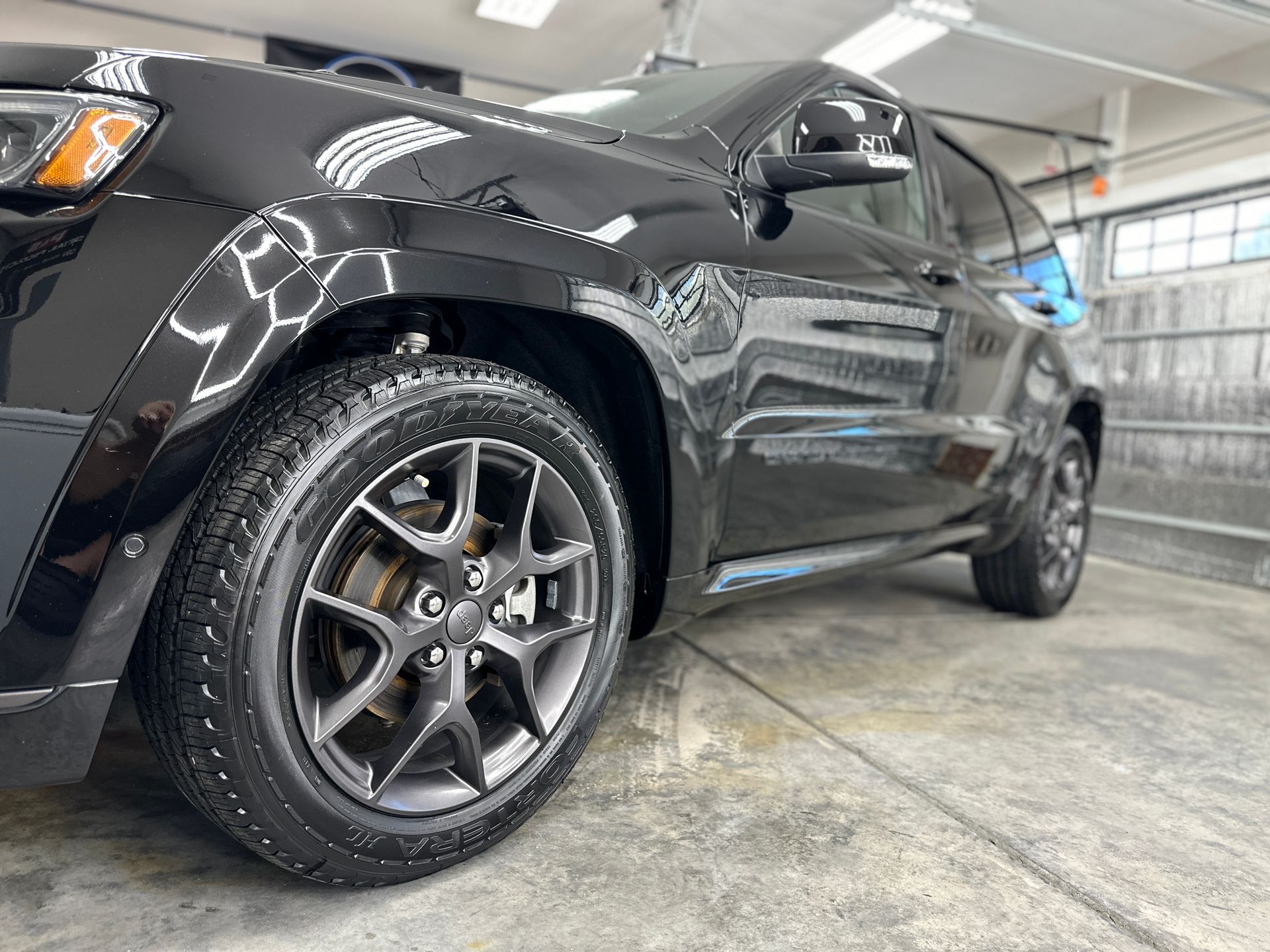 Black SUV with dark gray wheels, parked on a concrete surface, reflecting light.