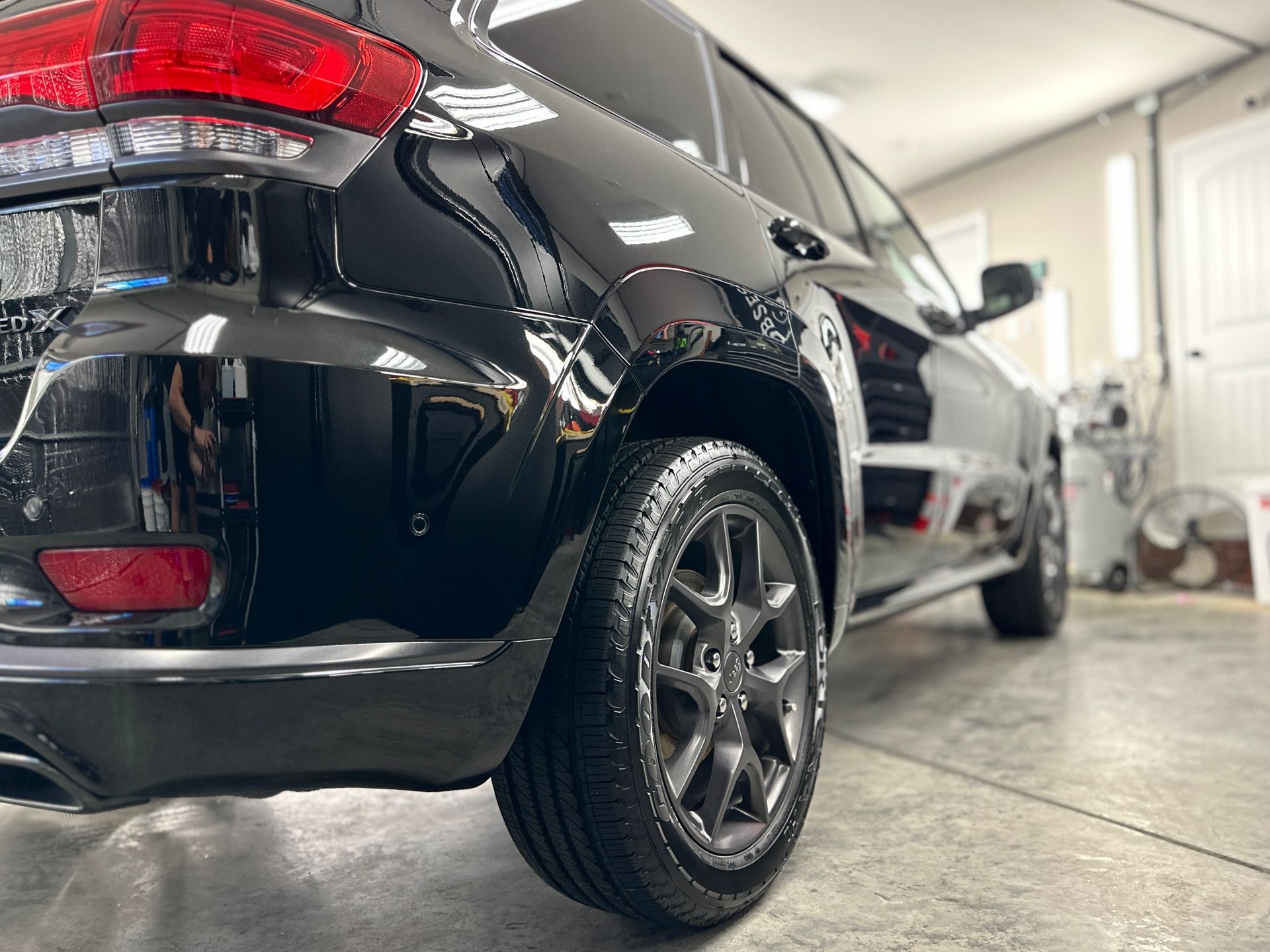 Black SUV parked inside a garage; focus on rear tire and taillight, shiny paint.