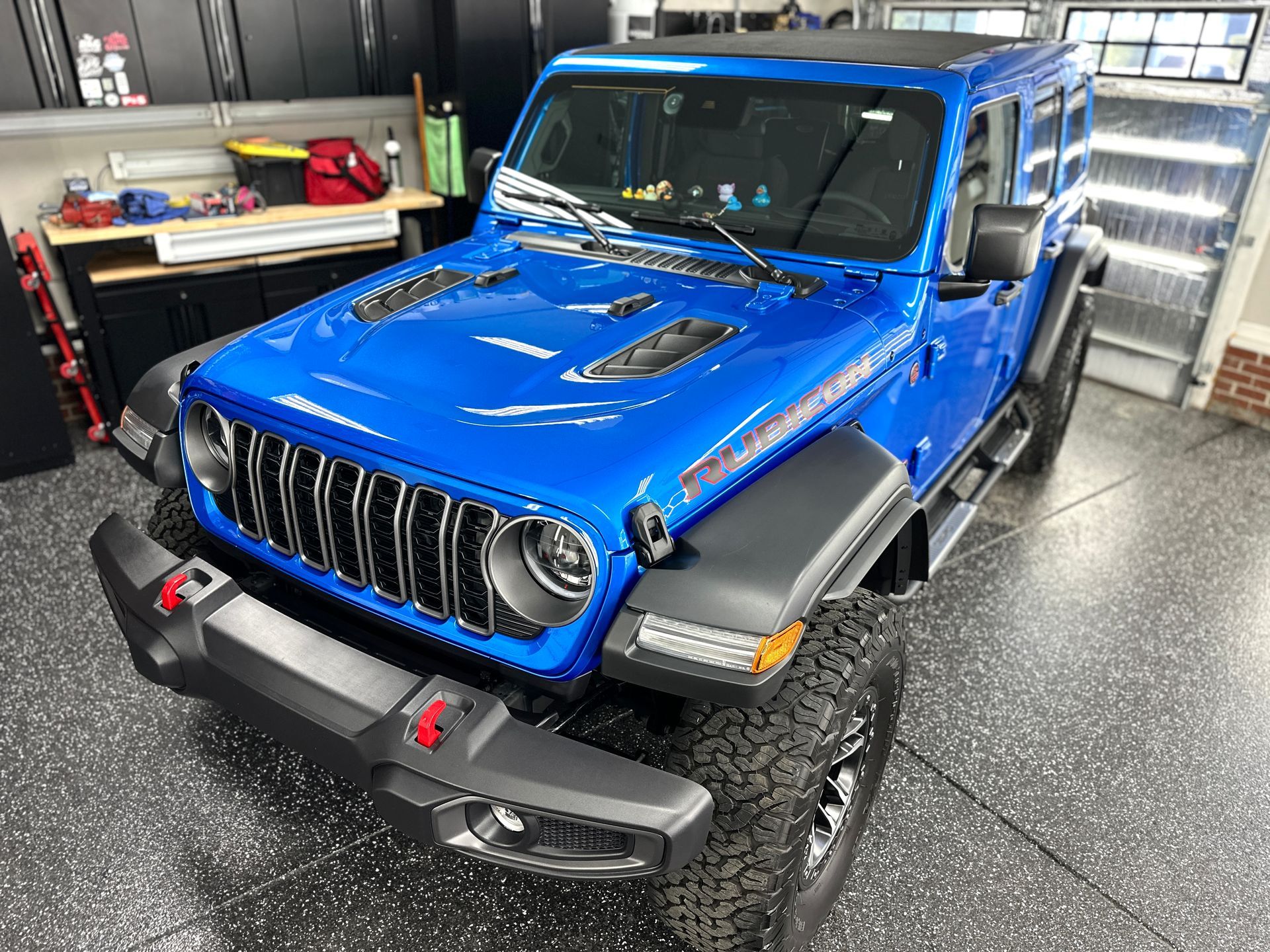Blue Jeep Wrangler Rubicon parked indoors. Black bumper, tires, and fender flares.