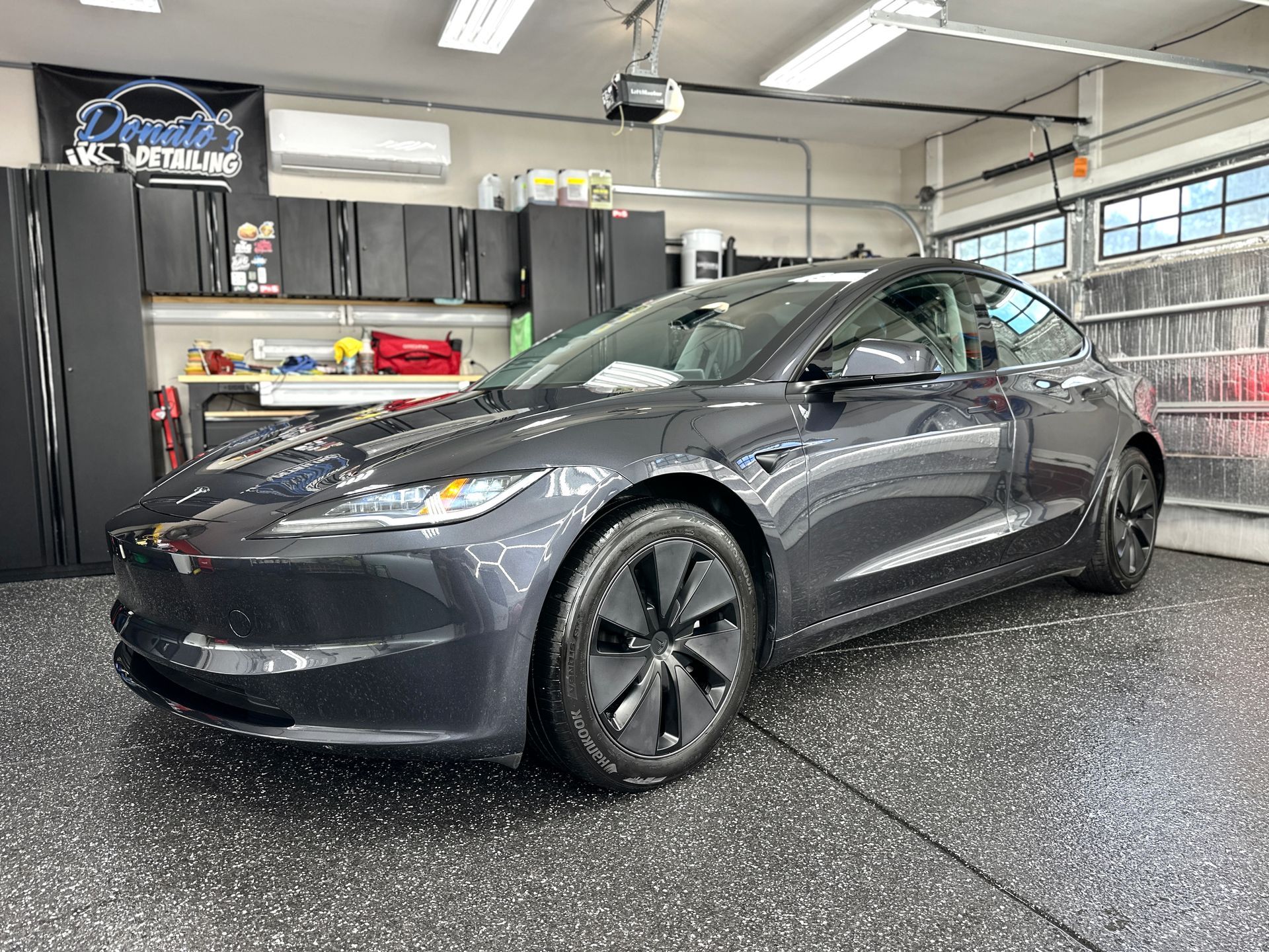 Dark gray Tesla car parked in a garage with black cabinets and a gray and black speckled floor.
