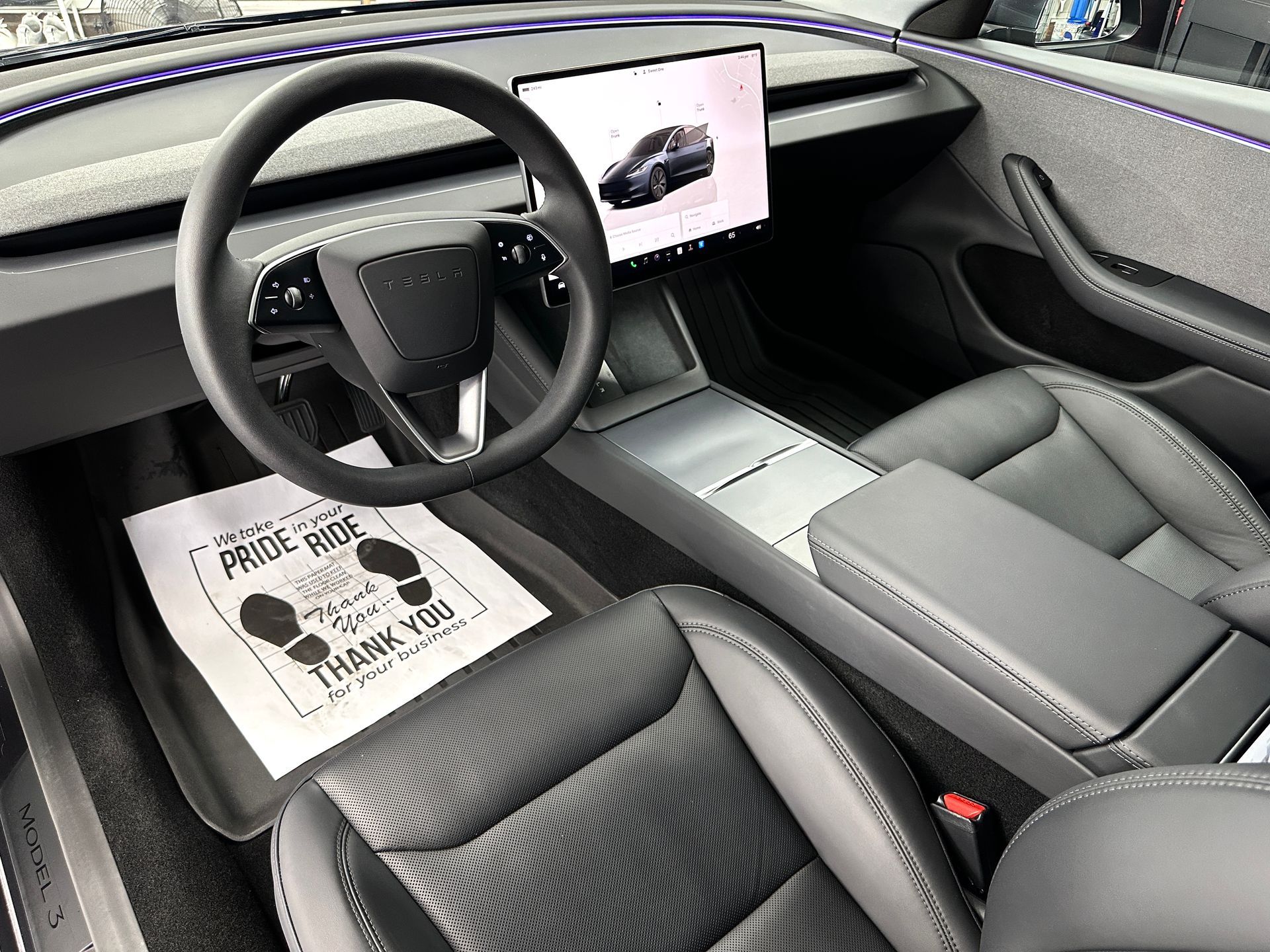 Interior of a gray car. Black leather seats, large touchscreen, steering wheel, and a center console.