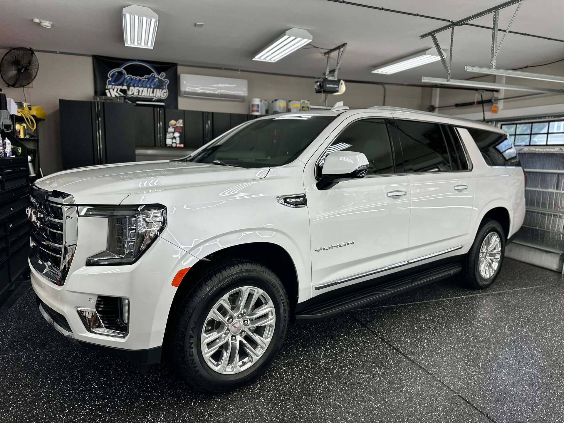White GMC Yukon SUV in a well-lit garage with black epoxy flooring.