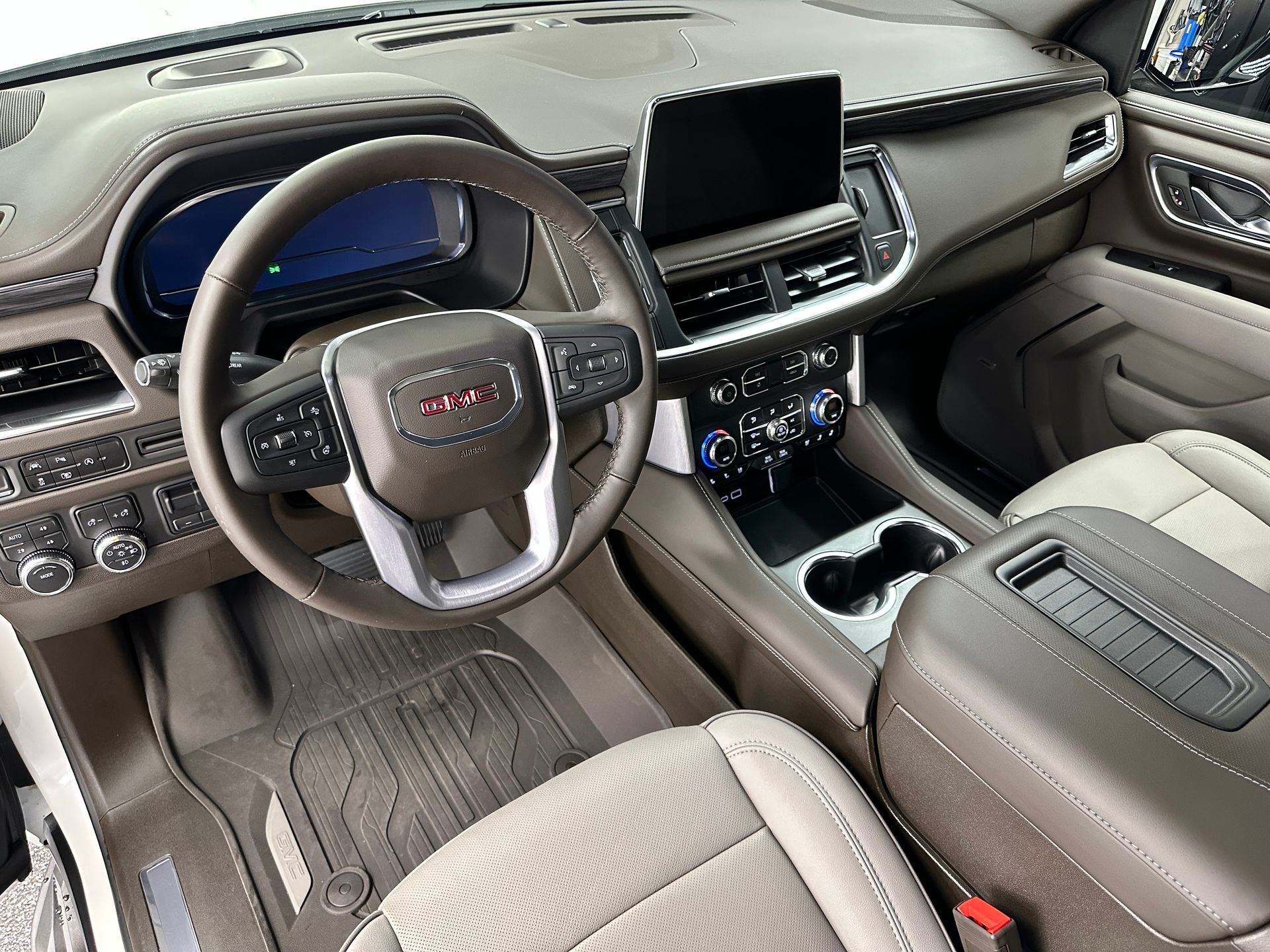 Interior view of a GMC vehicle: leather steering wheel, center console, infotainment screen, tan and brown color scheme.