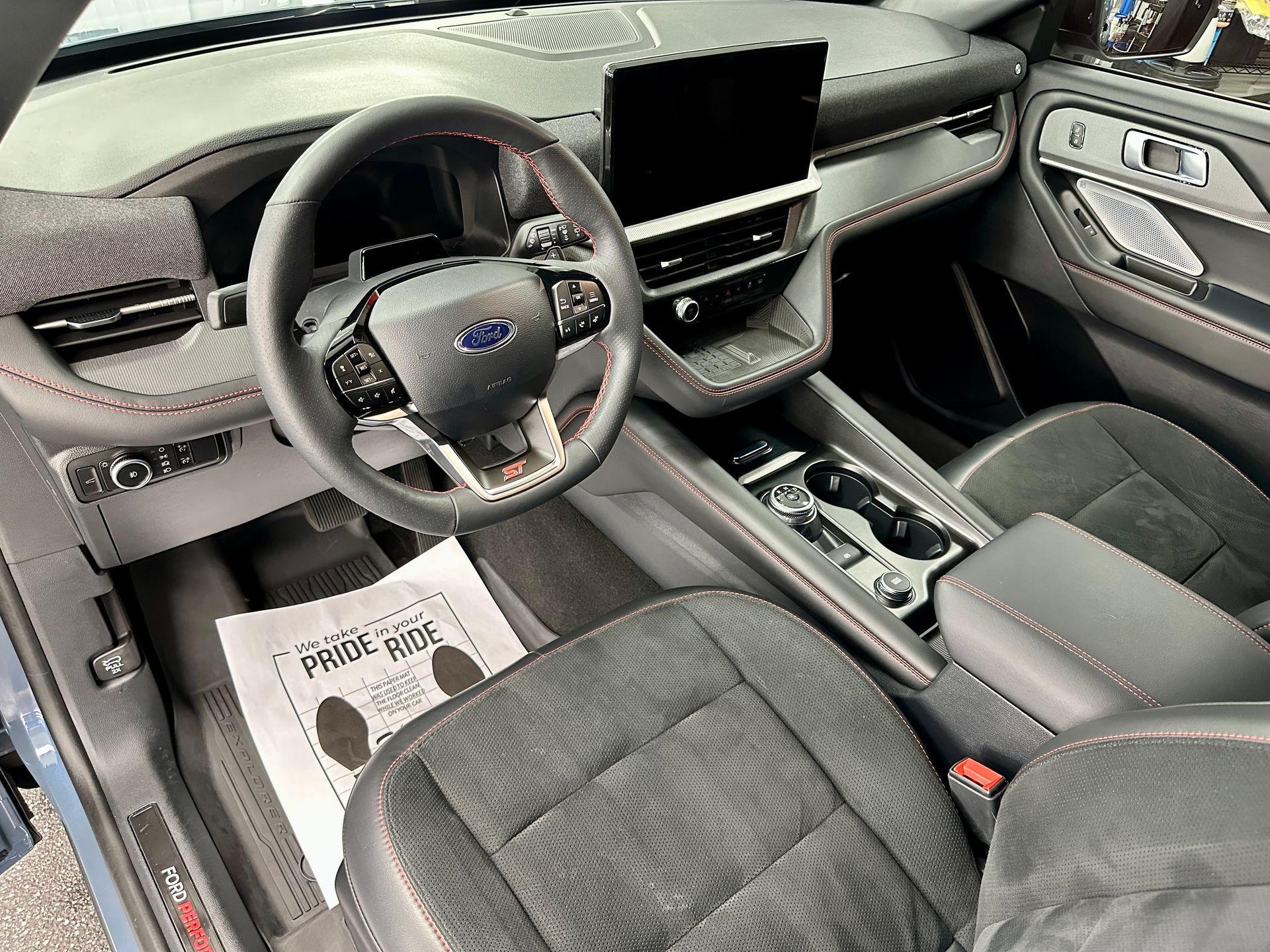 Interior of a car; dashboard, steering wheel, seats. Gray and black with red stitching accents.