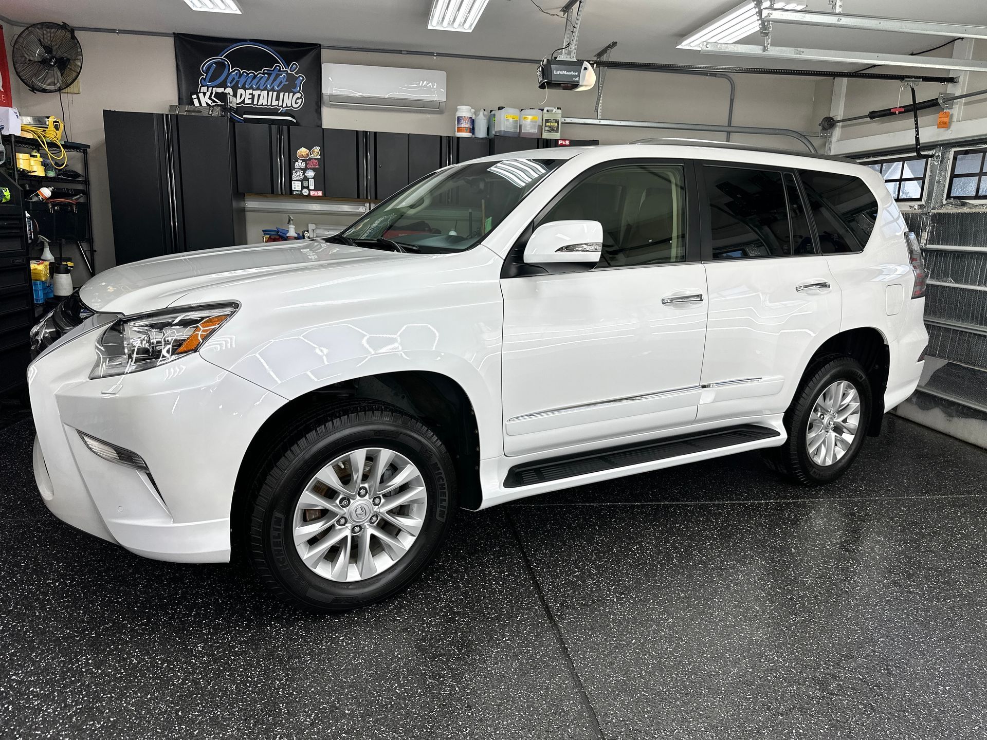 White Lexus GX SUV parked in a garage with black flooring and cabinets.