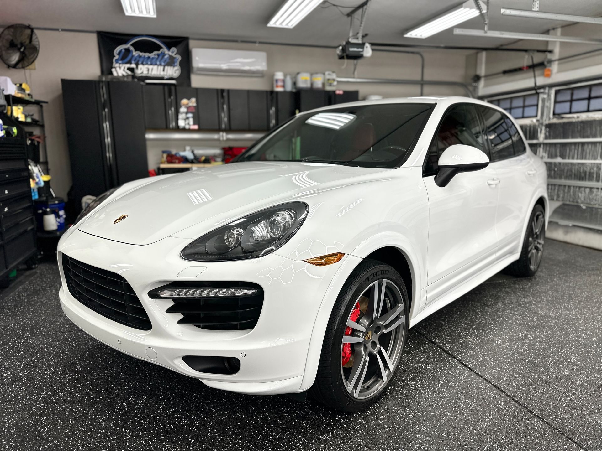 White Porsche SUV in a garage, with red brake calipers and black rims.