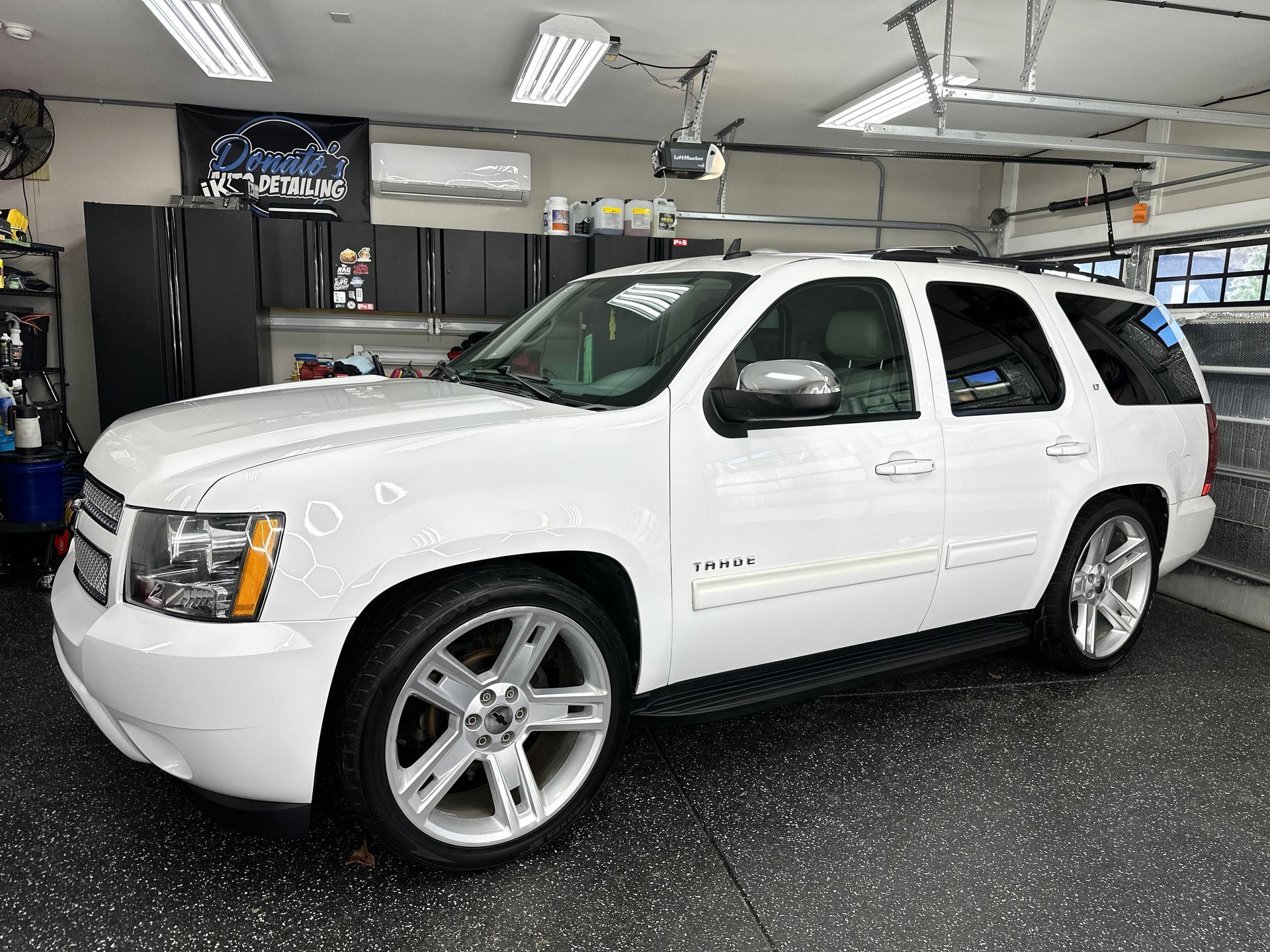 White Chevrolet Tahoe SUV parked inside a well-lit garage, with custom silver rims.