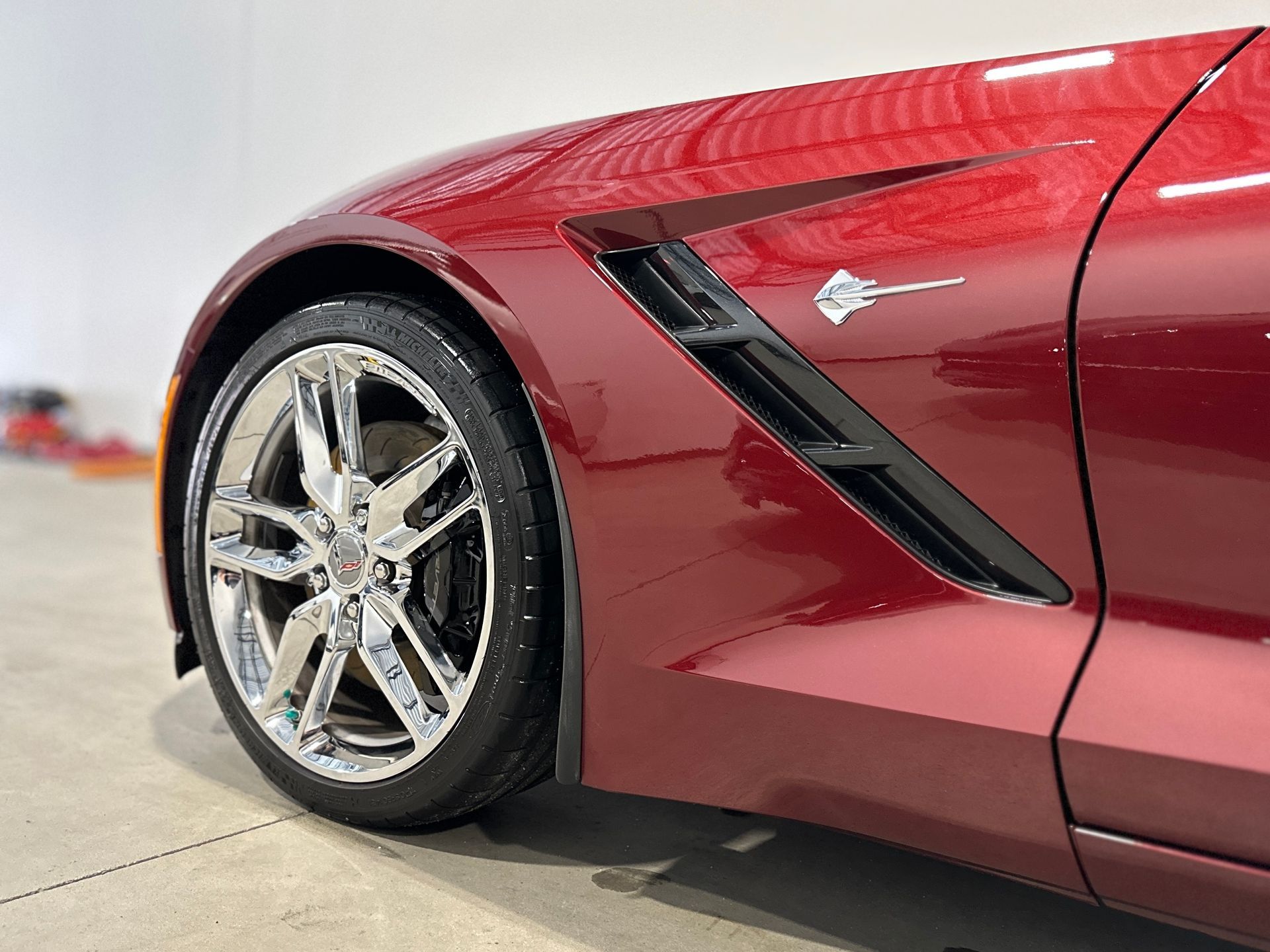 Red sports car side profile with chrome wheels, black vent, and Corvette emblem.