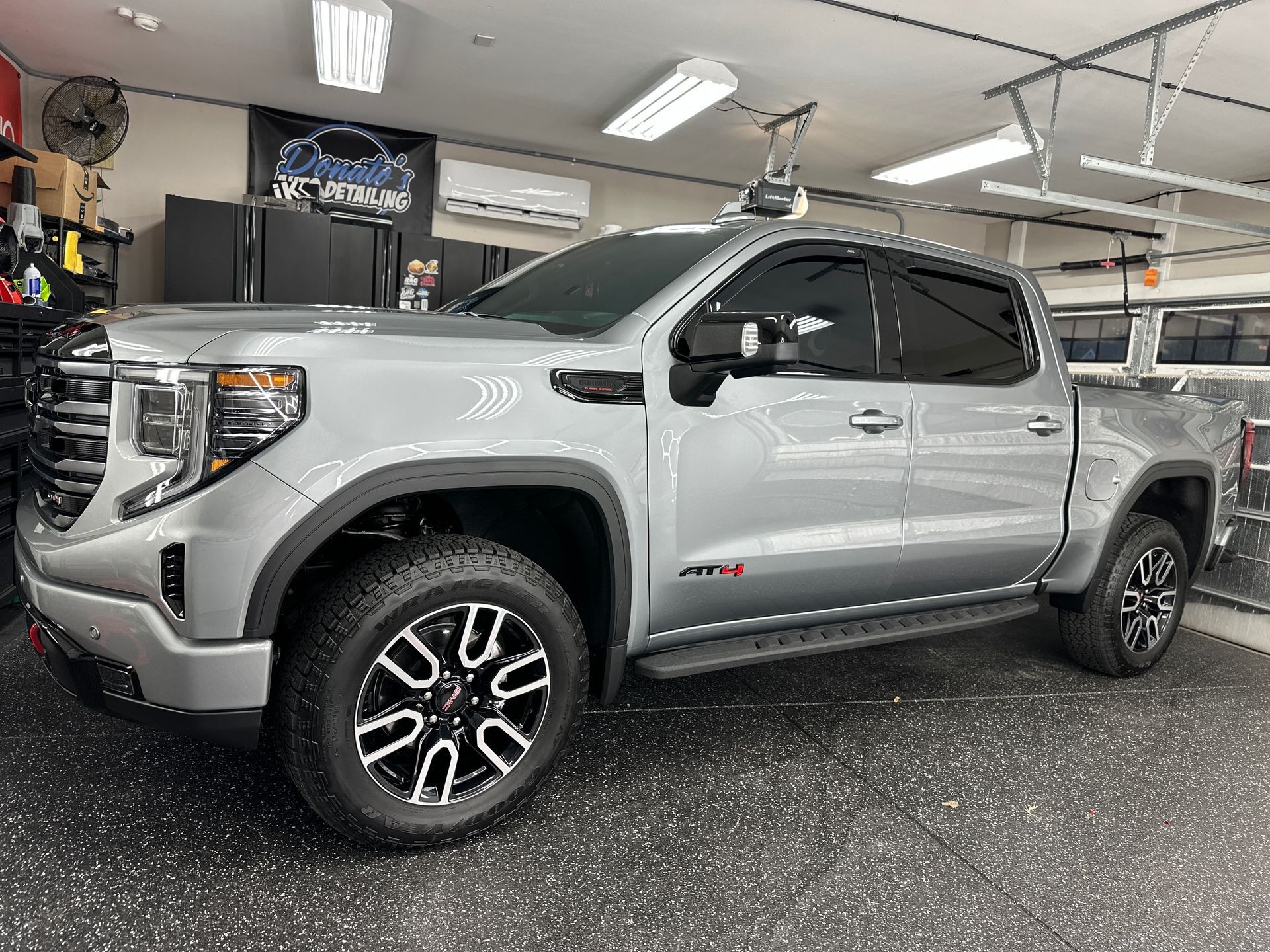Silver GMC Sierra AT4 truck parked in a garage with tinted windows and black and silver wheels.