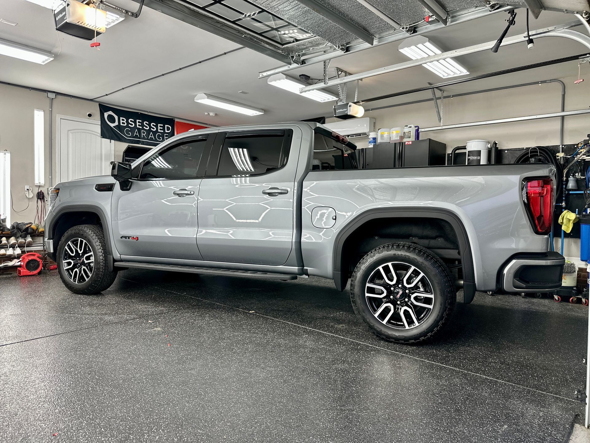 Gray GMC truck in a garage with black and white wheels.