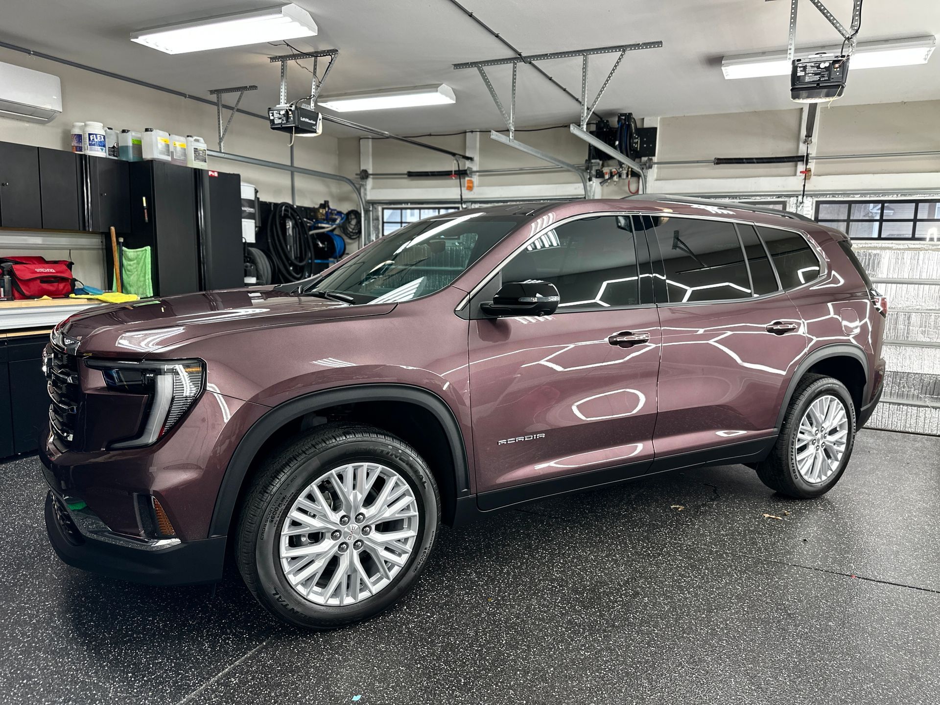 A maroon GMC SUV parked inside a well-lit garage, with shiny wheels and tinted windows.