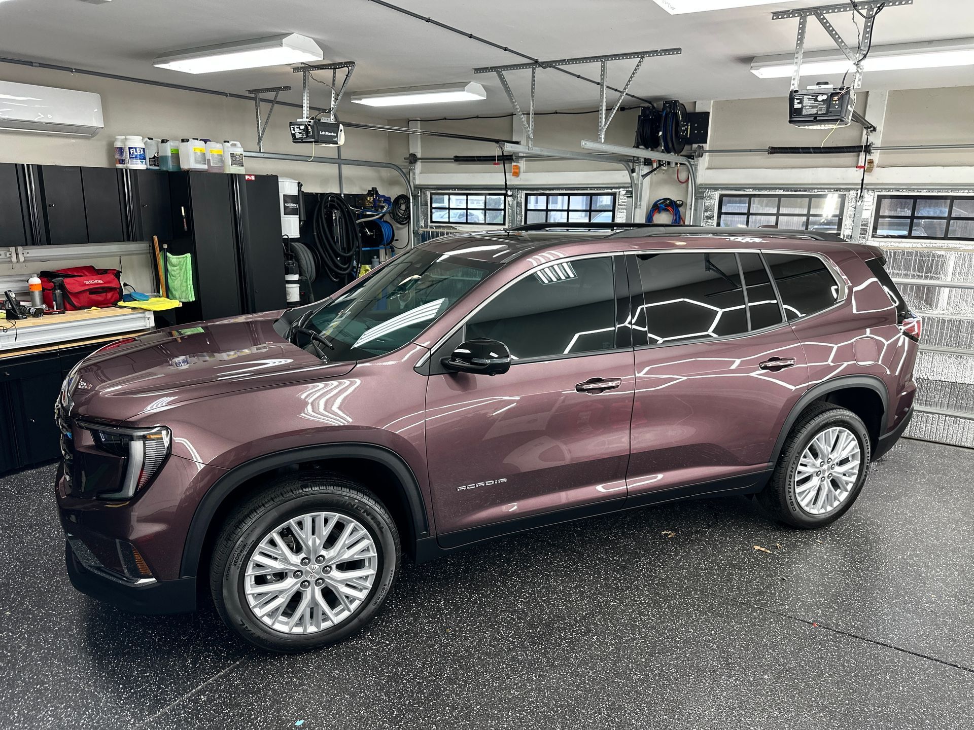 A maroon SUV parked inside a garage. The garage has black cabinets and a patterned epoxy floor.