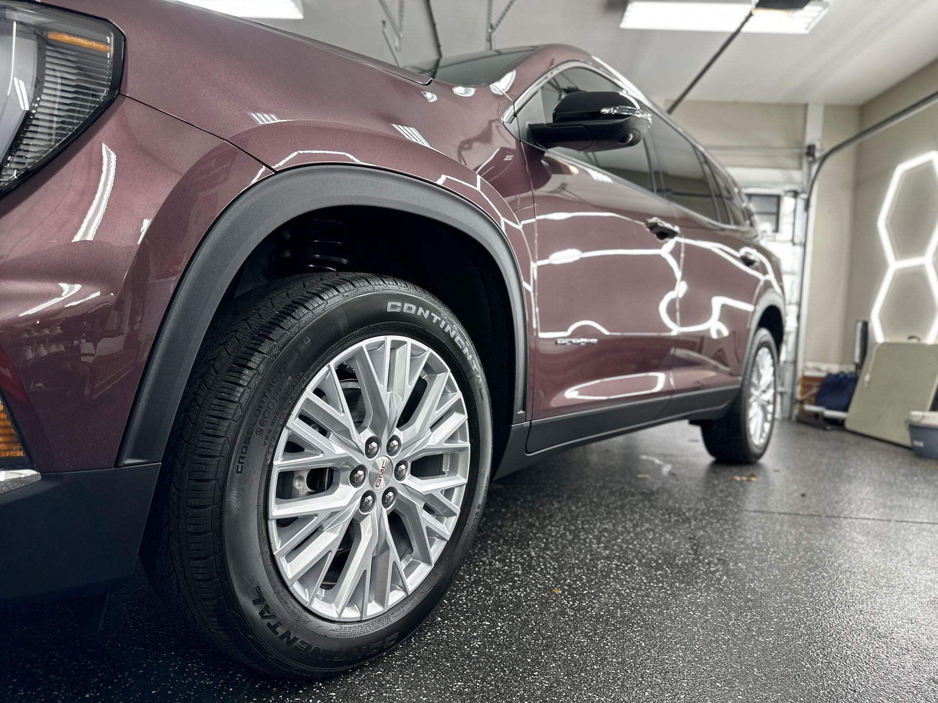 Dark red SUV parked in a car wash bay, with wet black flooring and bright lights.