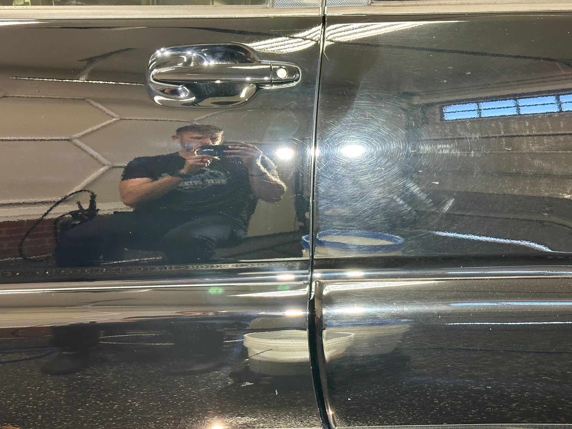 Shiny black car door reflecting a person taking a photo in a garage.