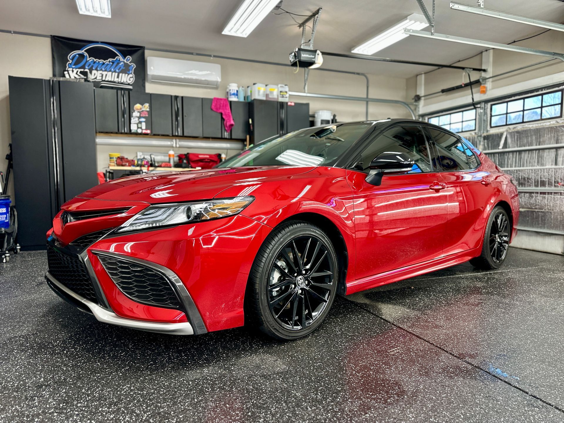 Red Toyota Camry in a garage, black rims, black roof, and black accents.