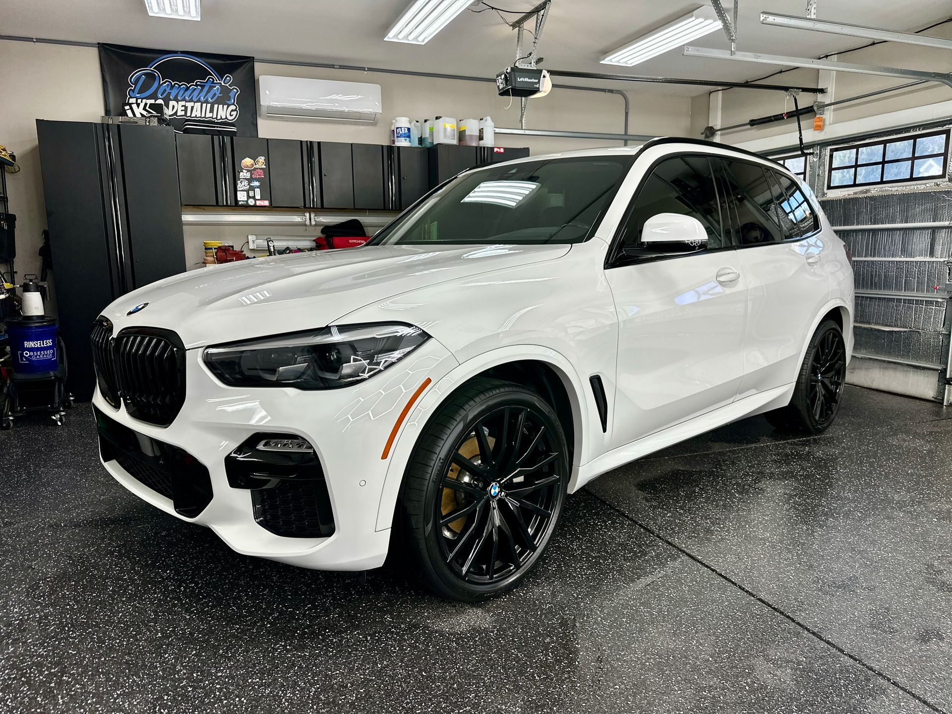 White BMW X5 SUV in a garage with black rims, shiny finish.