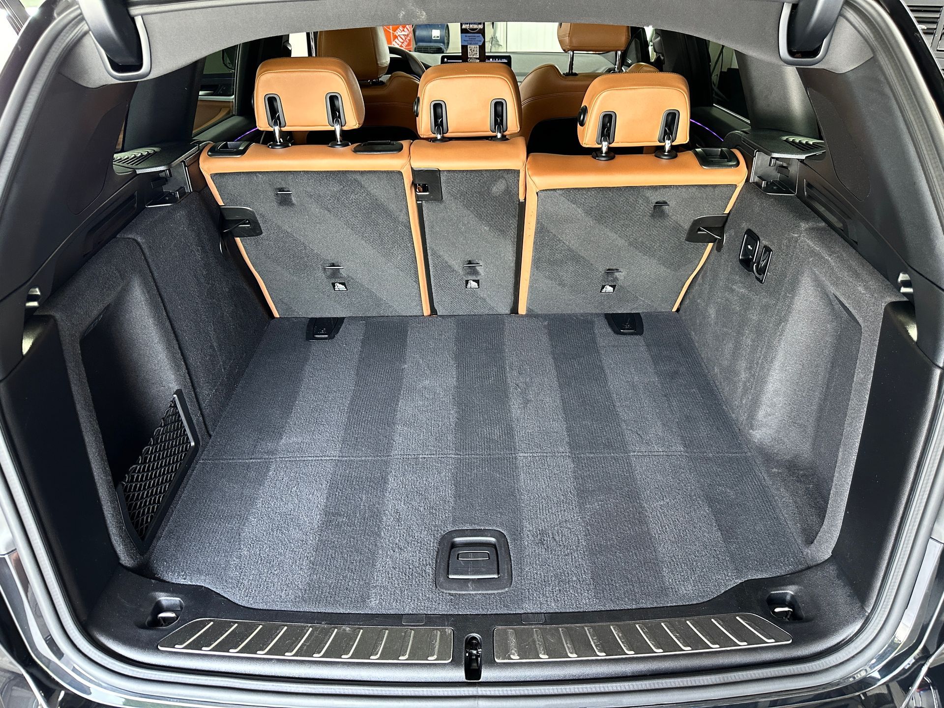 Clean, empty car trunk with gray carpet and tan back seats.