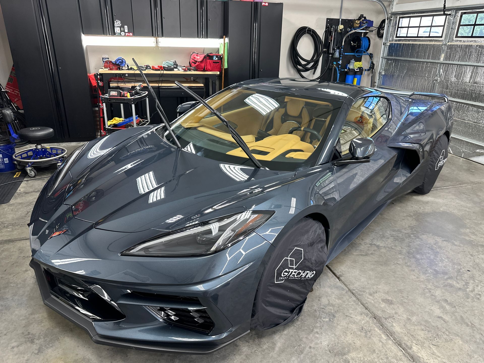 Gray Corvette sports car in a garage, car covers on wheels, tan interior.