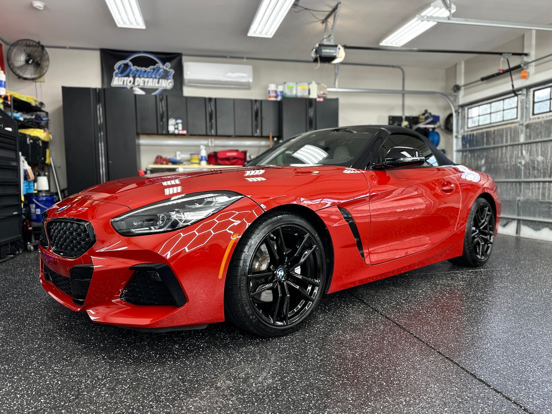 Red BMW Z4 convertible parked in a garage with black cabinets and a black and gray floor.