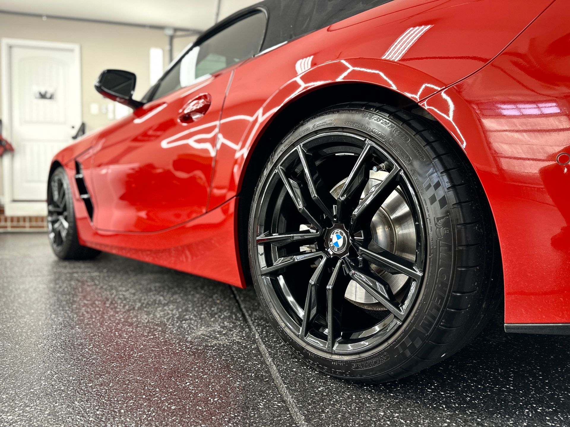 Red BMW convertible with black rims parked on a speckled garage floor.
