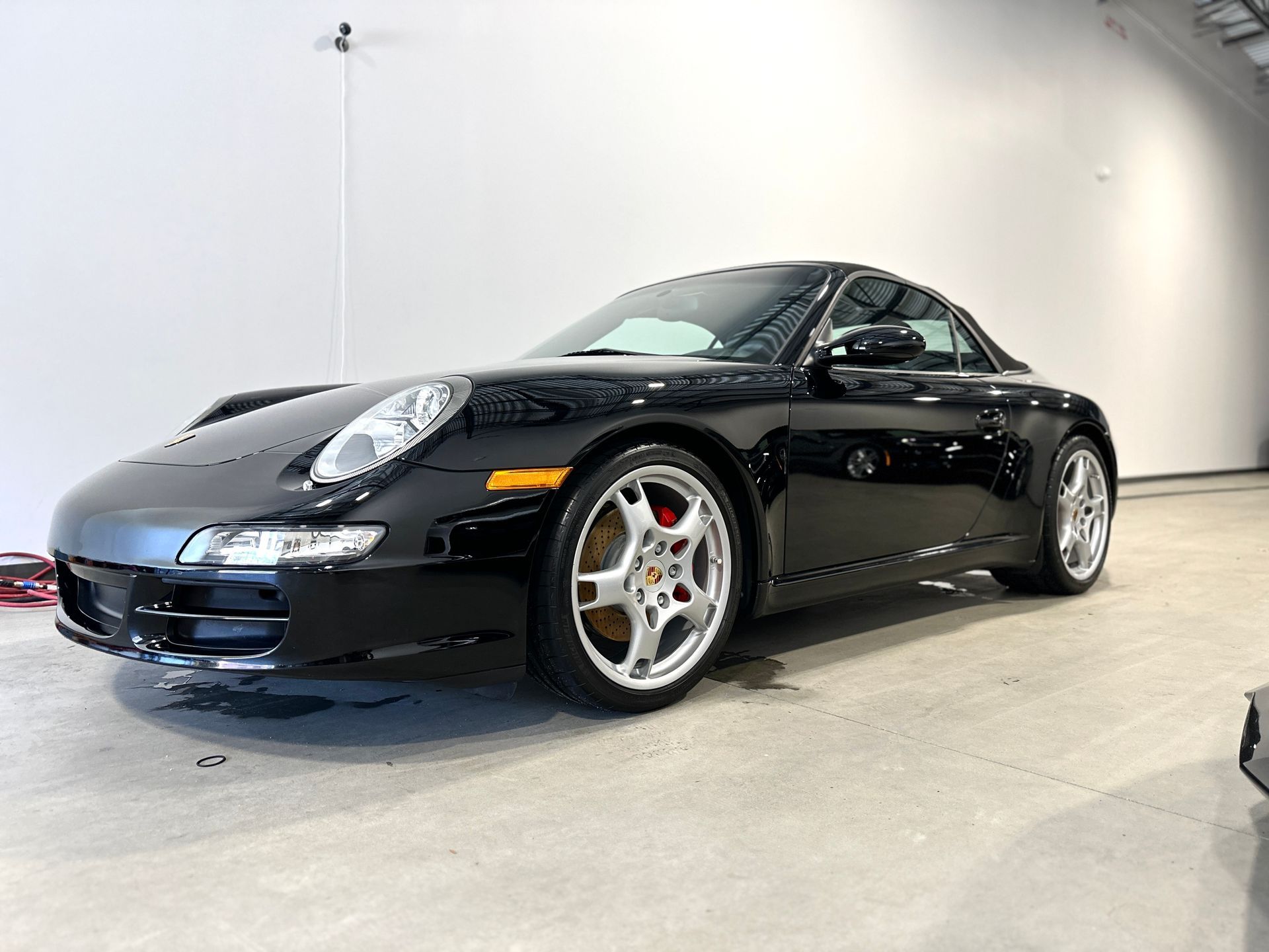 Black Porsche sports car parked indoors, angled view. Silver wheels, red brake calipers.