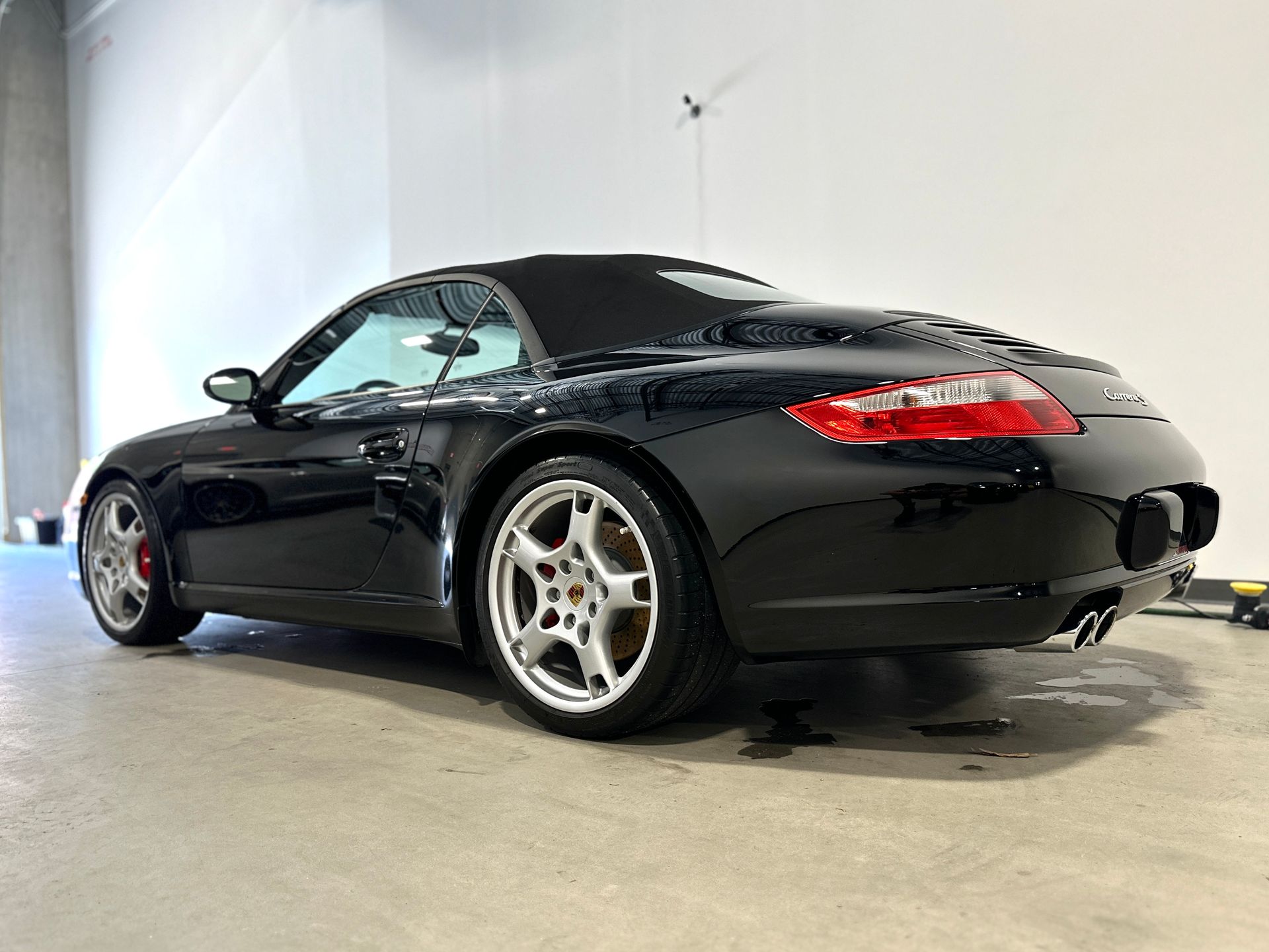 Black Porsche convertible parked in a white-walled garage, showing off its curves and alloy wheels.