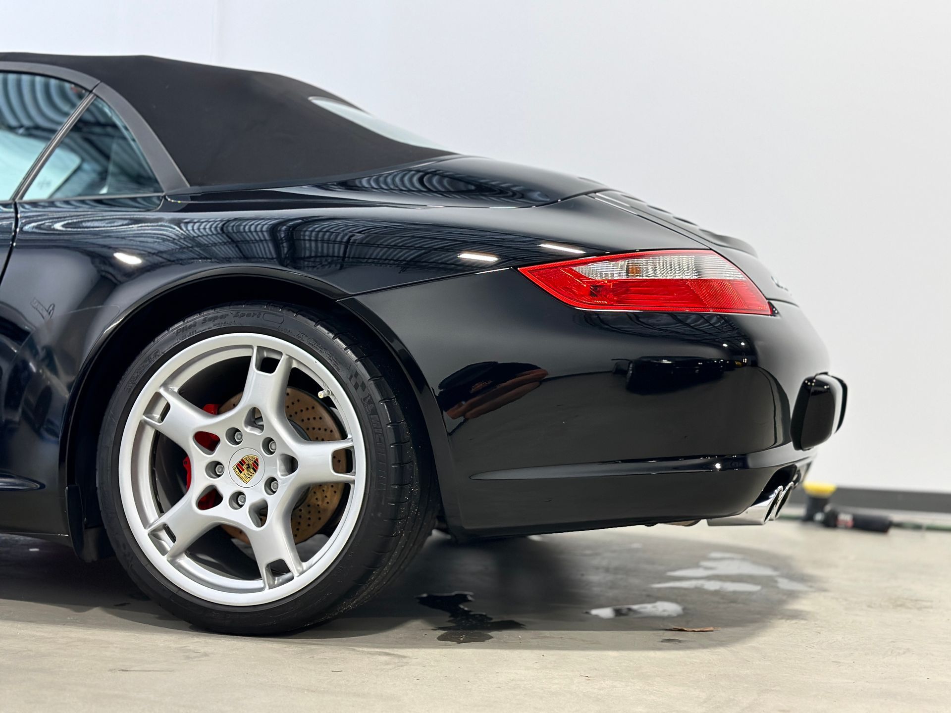 Black Porsche convertible, rear view, silver wheels, red brake calipers.