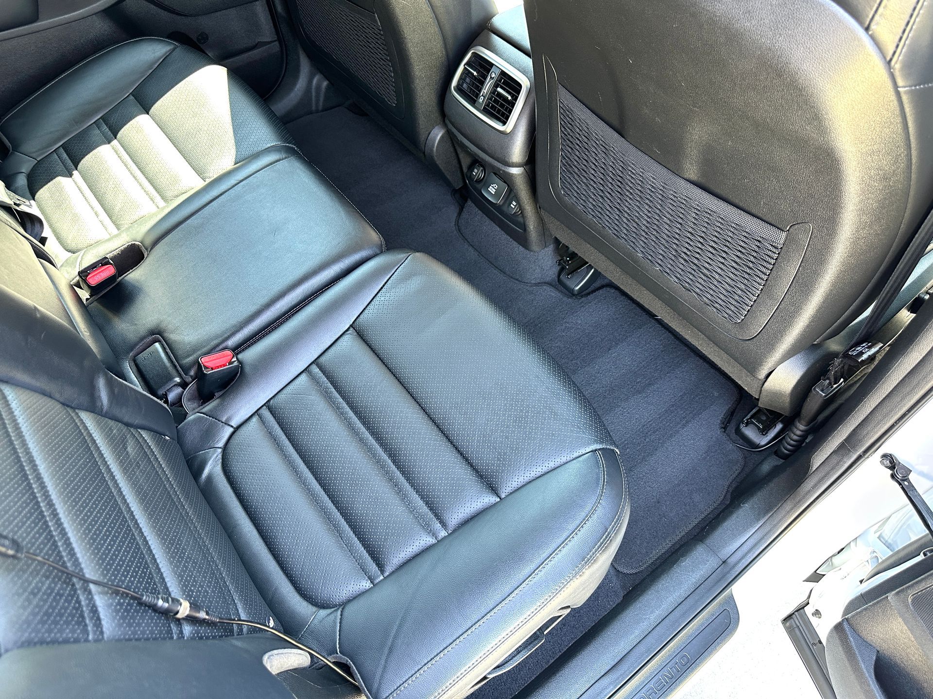 Black leather car backseat with a black carpet floor.