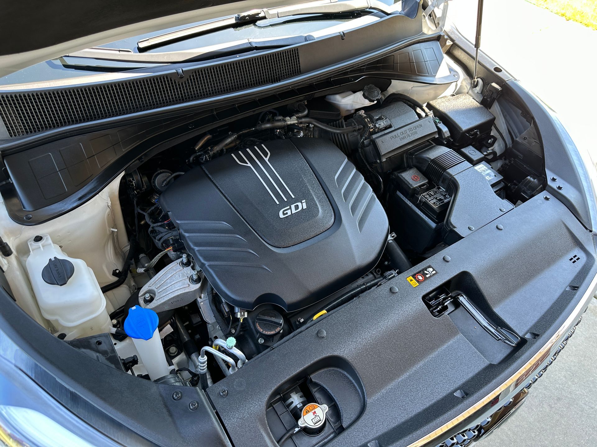 Kia engine bay with black engine cover, GDI logo, and various components.