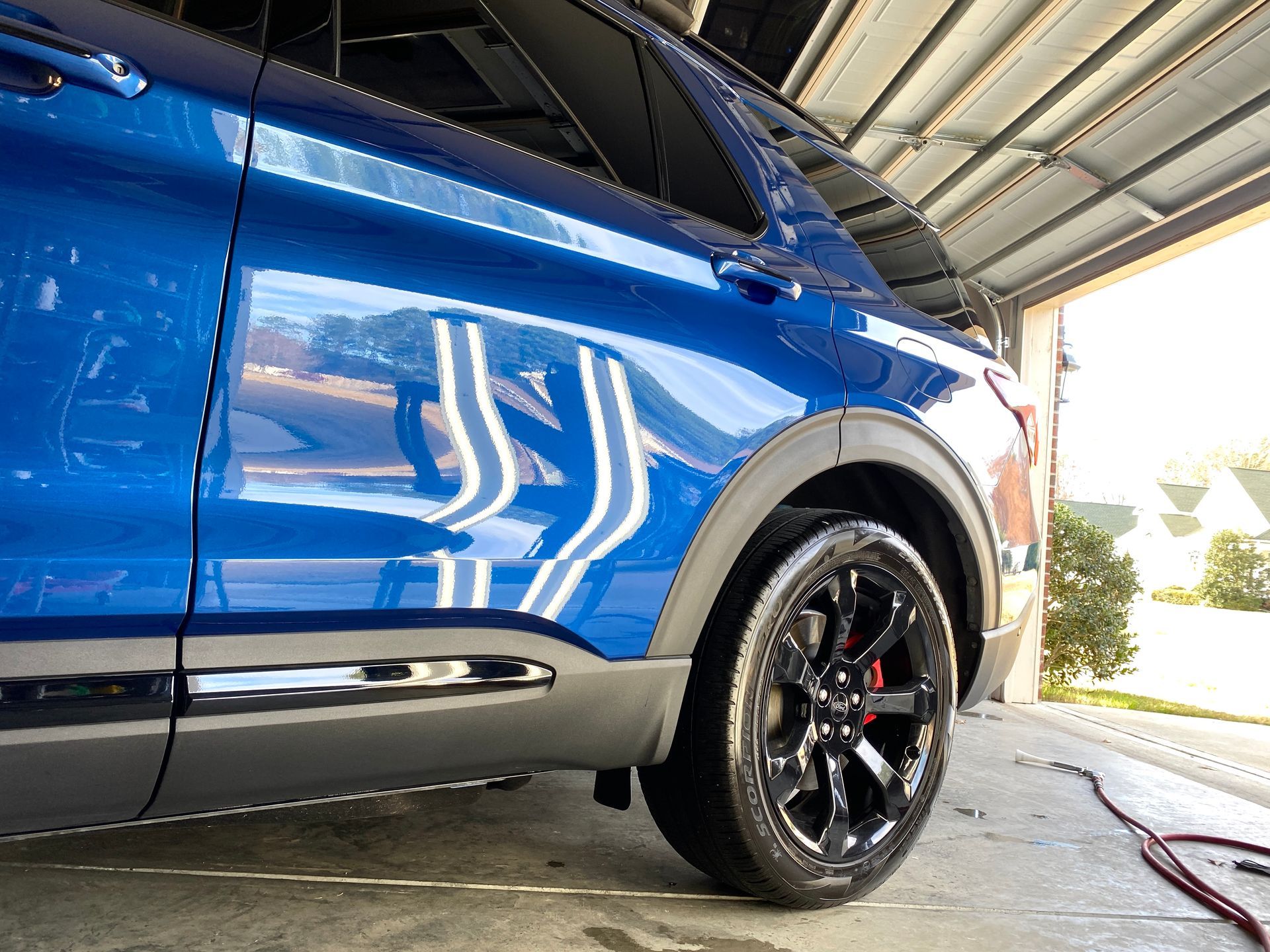 Blue SUV parked inside a garage; the car's glossy finish reflects white stripes.