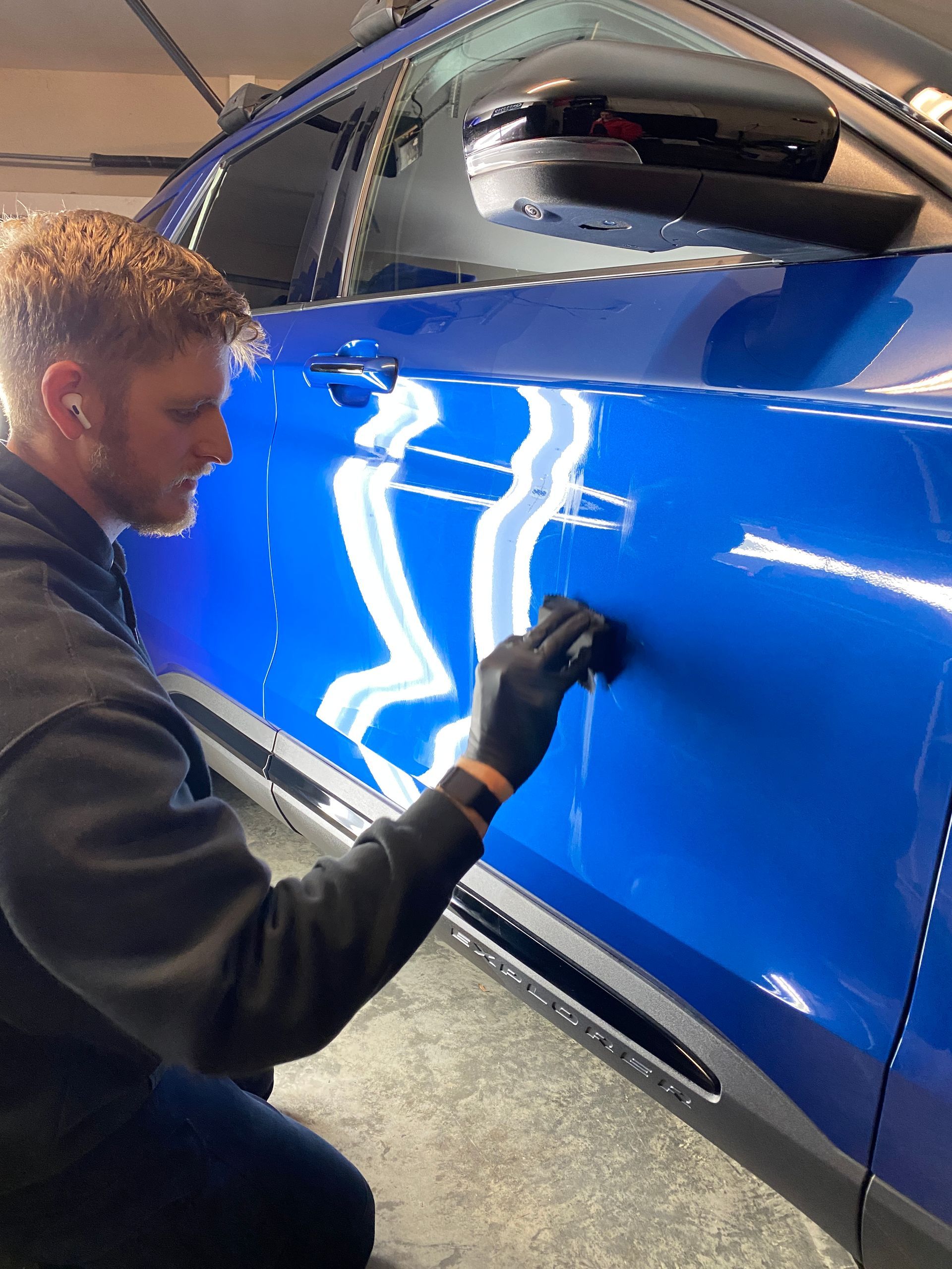 Person polishing a bright blue car door with a black glove.
