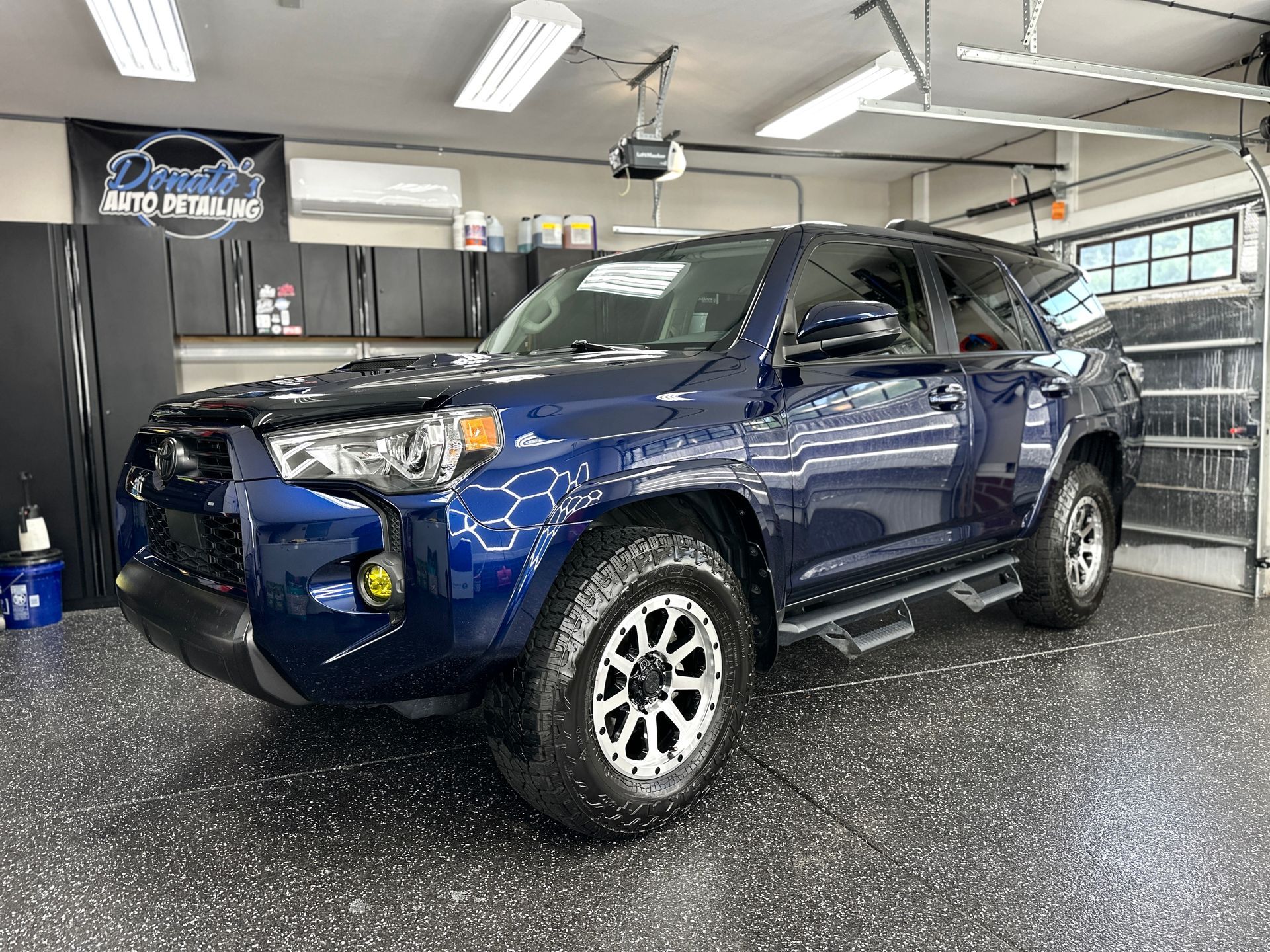 Blue Toyota 4Runner SUV inside a garage, tires on patterned floor, under bright lights.