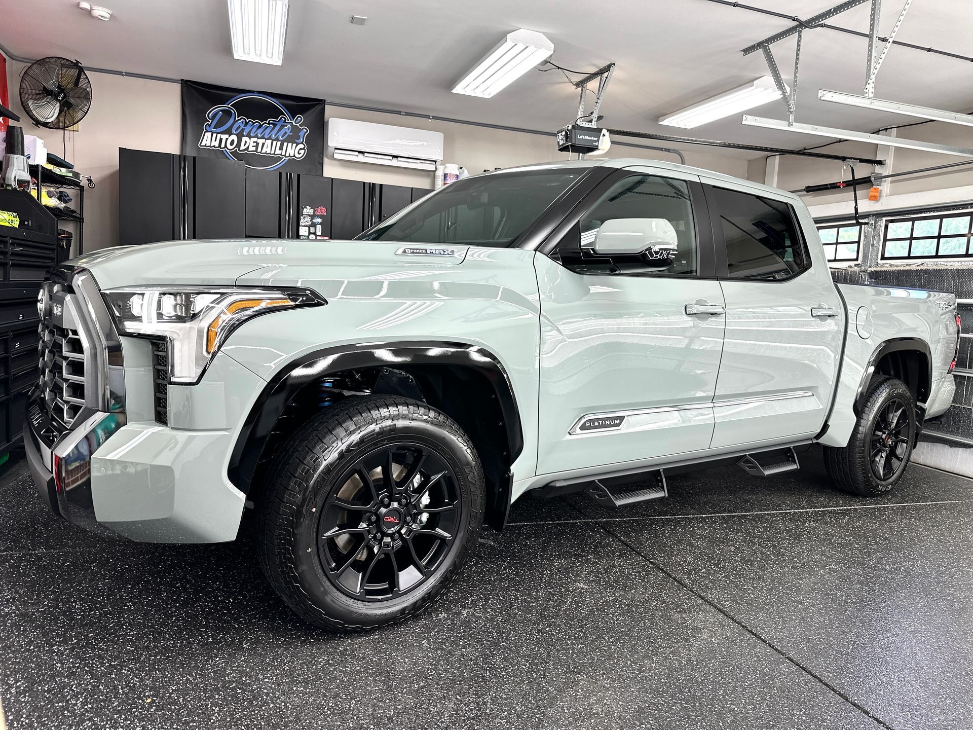Light green Toyota Tundra truck with black rims parked in a garage with black floor tiles.
