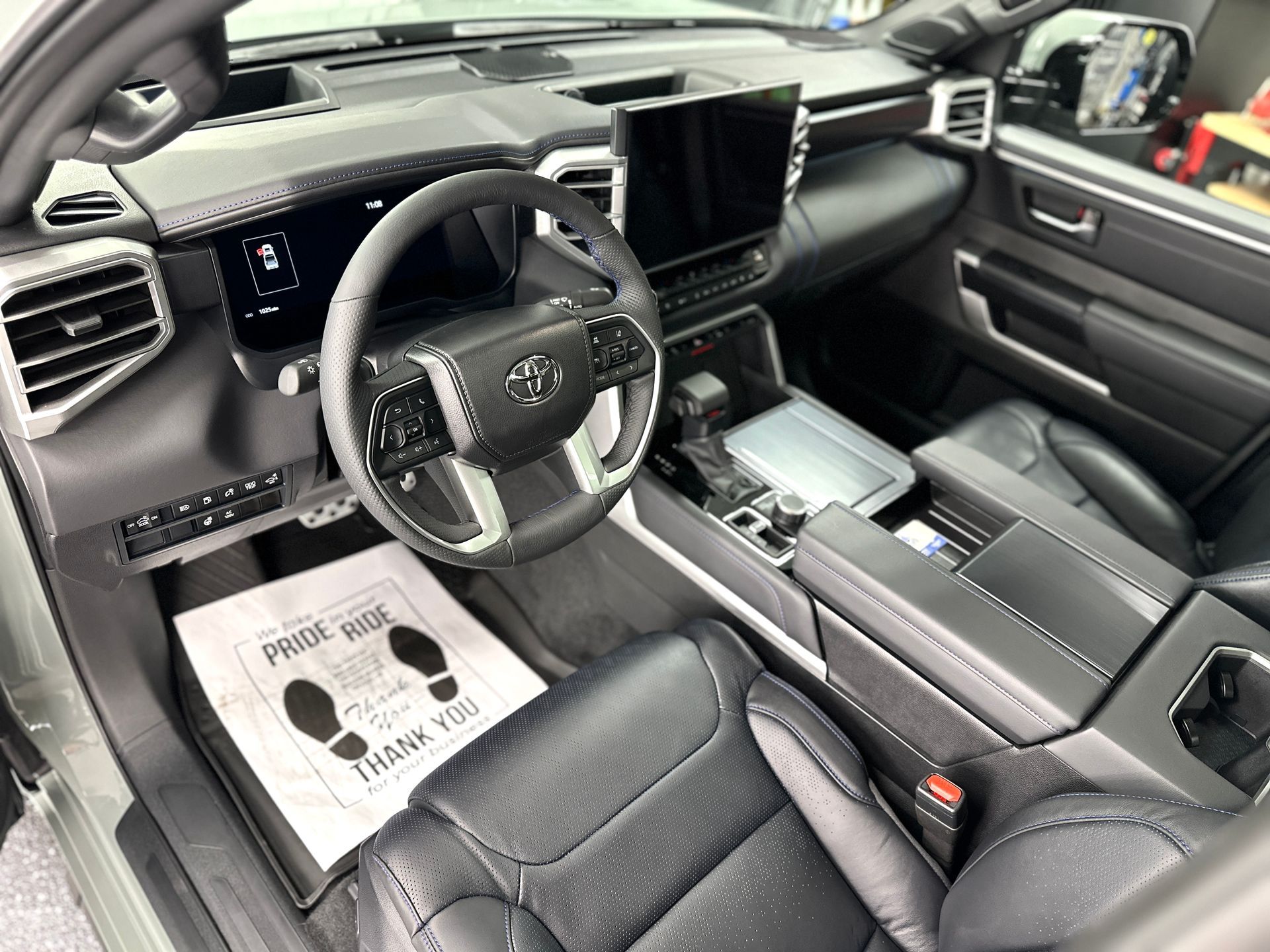 Black leather interior of a Toyota Tundra truck with dashboard, steering wheel, and a “Pride Ride” floor mat.