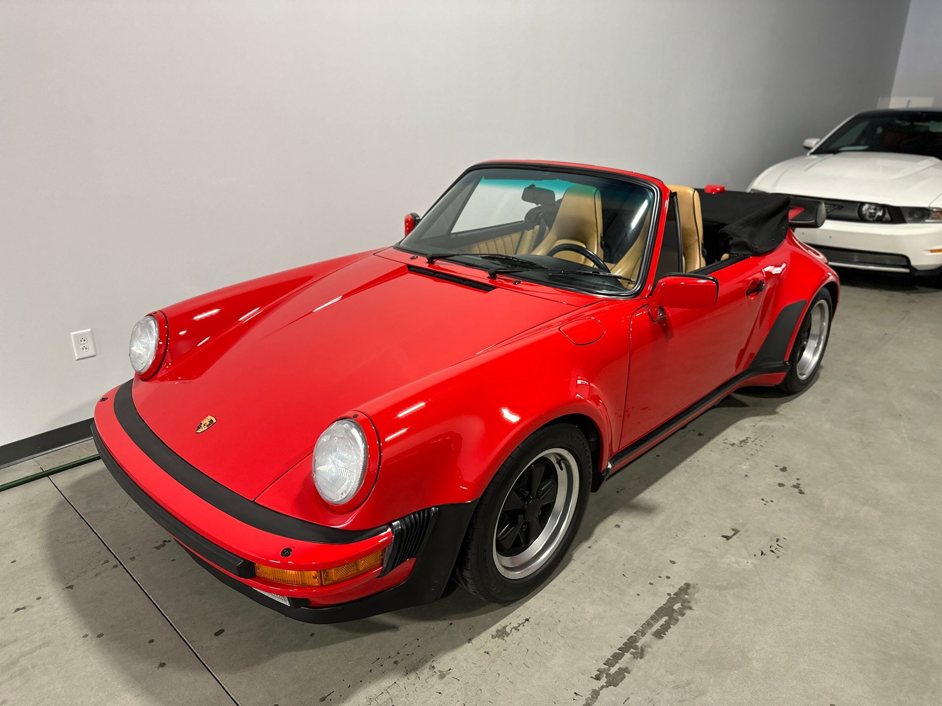 Red Porsche 911 convertible with black wheels, tan interior, parked indoors.