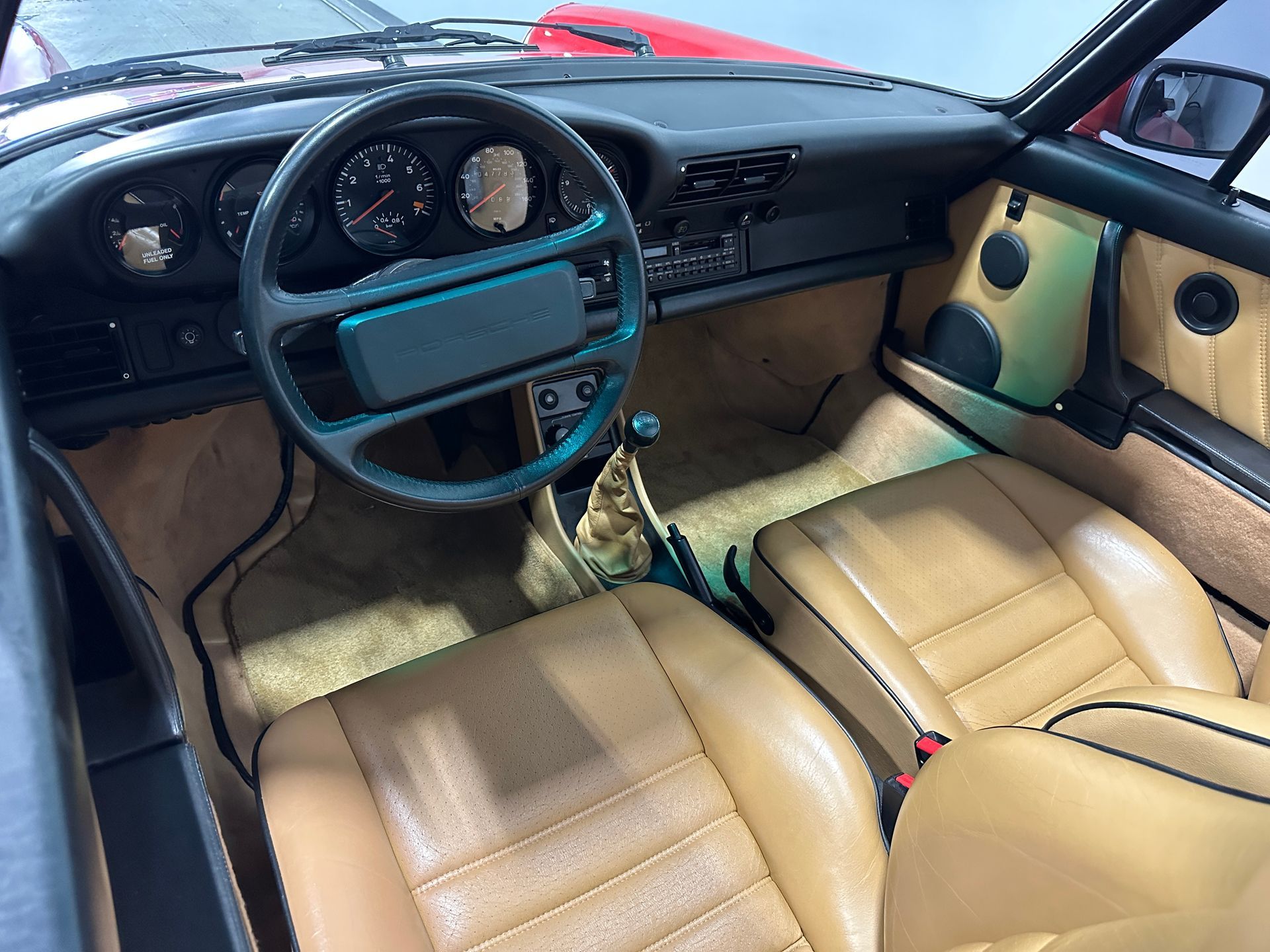 Tan leather interior of a vintage Porsche sports car; dashboard, steering wheel, and seats visible.