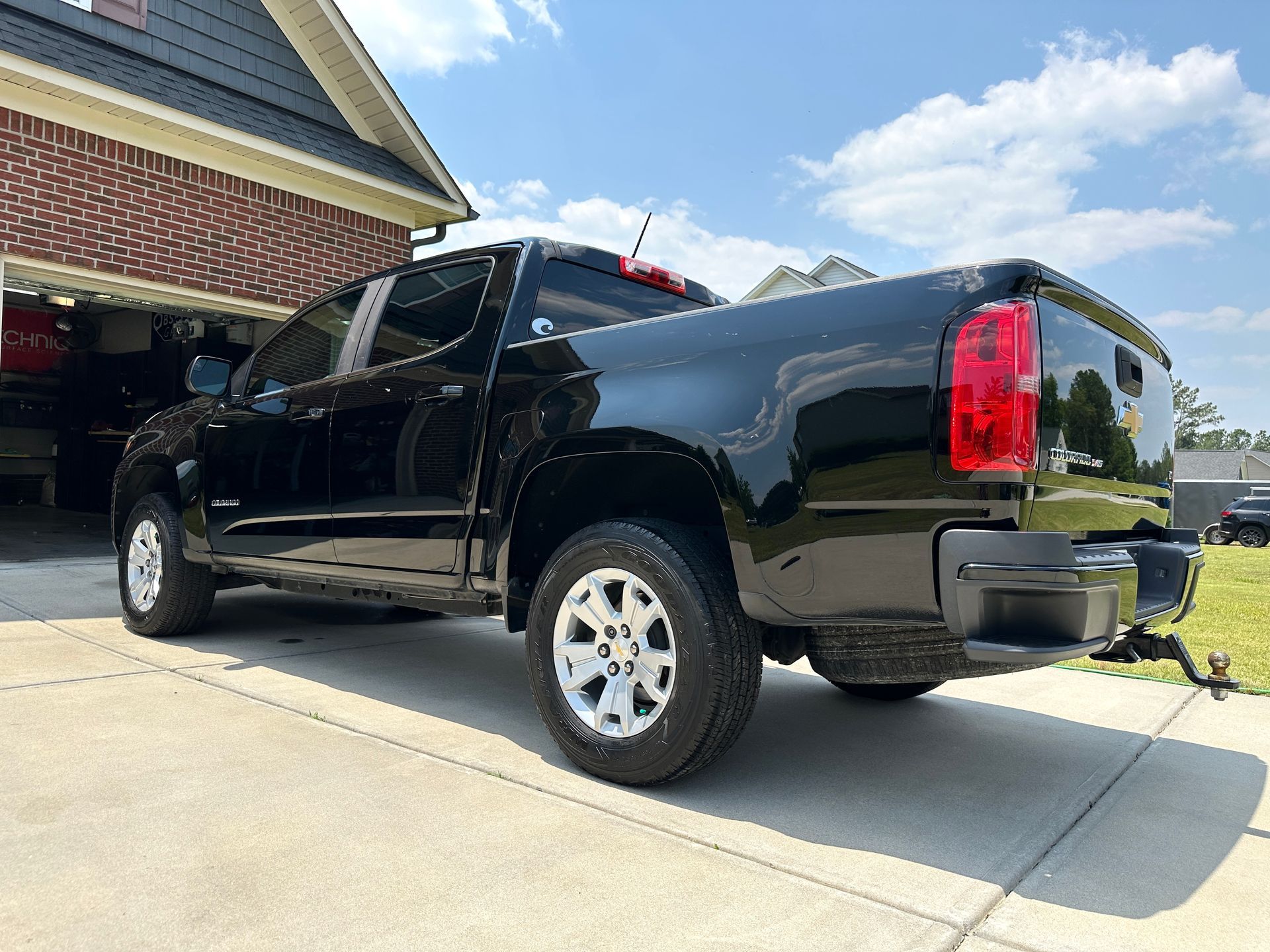 Black Chevrolet Colorado truck parked on a driveway in front of a house on a sunny day.