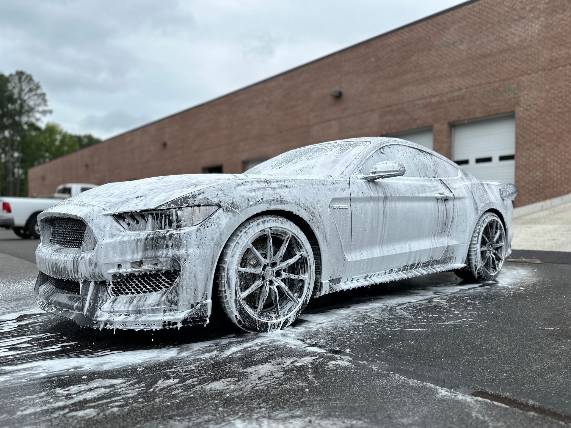Ford Mustang covered in white foam, parked in front of a brick building.