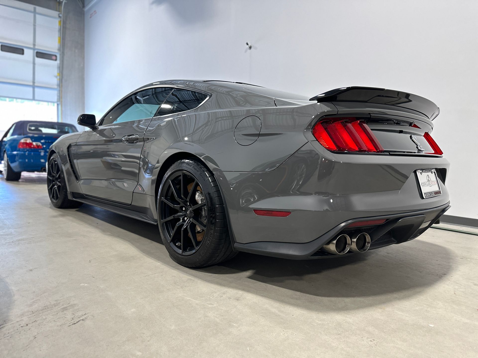 Gray Ford Mustang sports car with black wheels and spoiler, parked indoors.