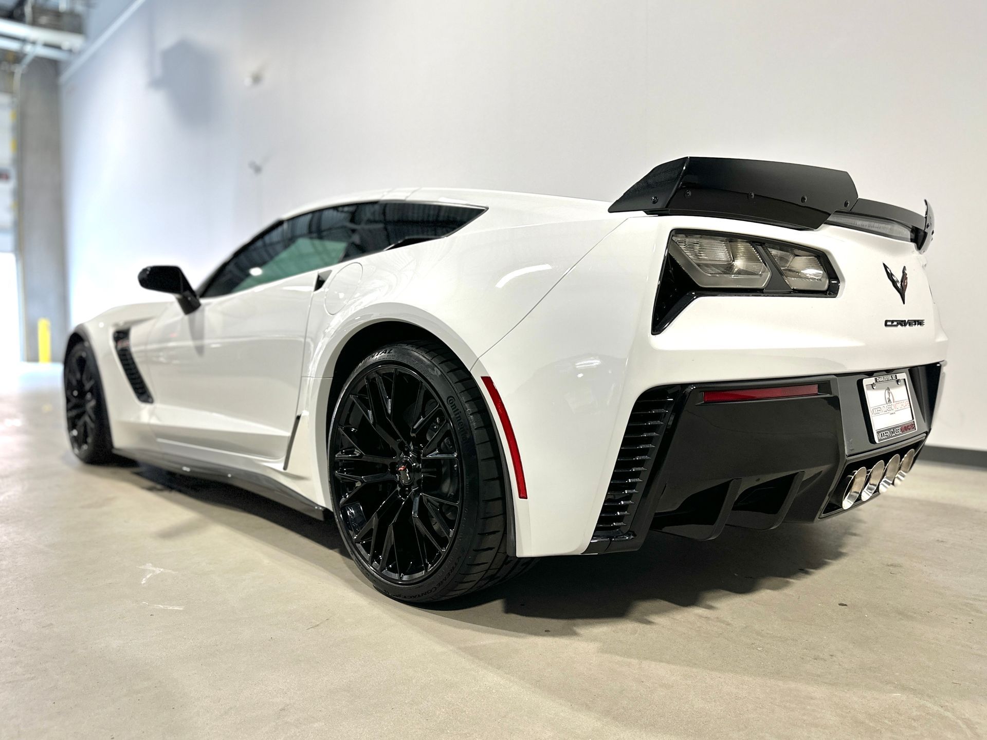 White sports car with black accents and spoiler, parked indoors.