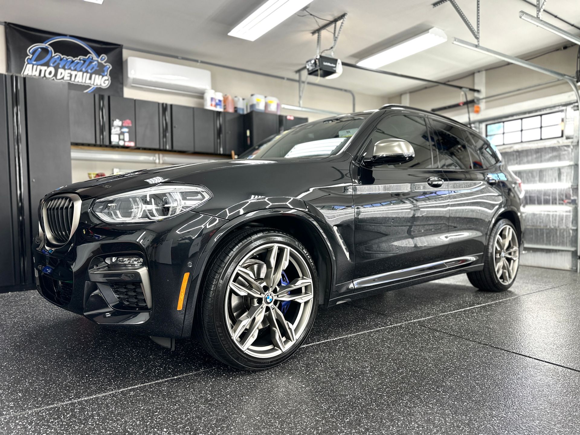 Black BMW X3 SUV in a garage with detailing equipment.