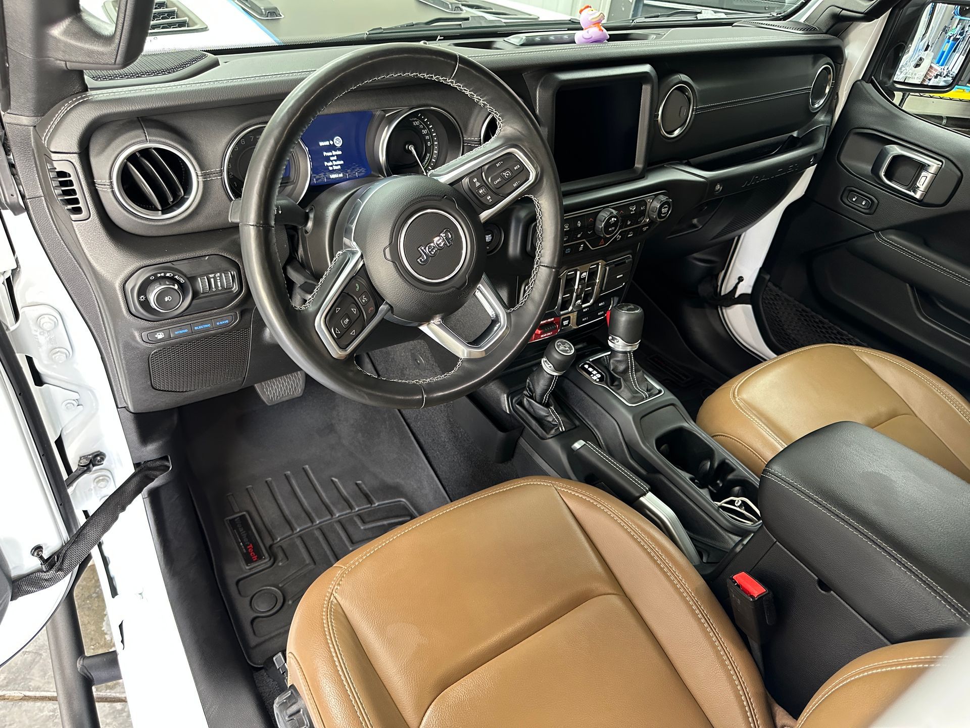 Interior of a Jeep Wrangler: white, black, and tan dashboard, steering wheel, seats, and WeatherTech floor mats.