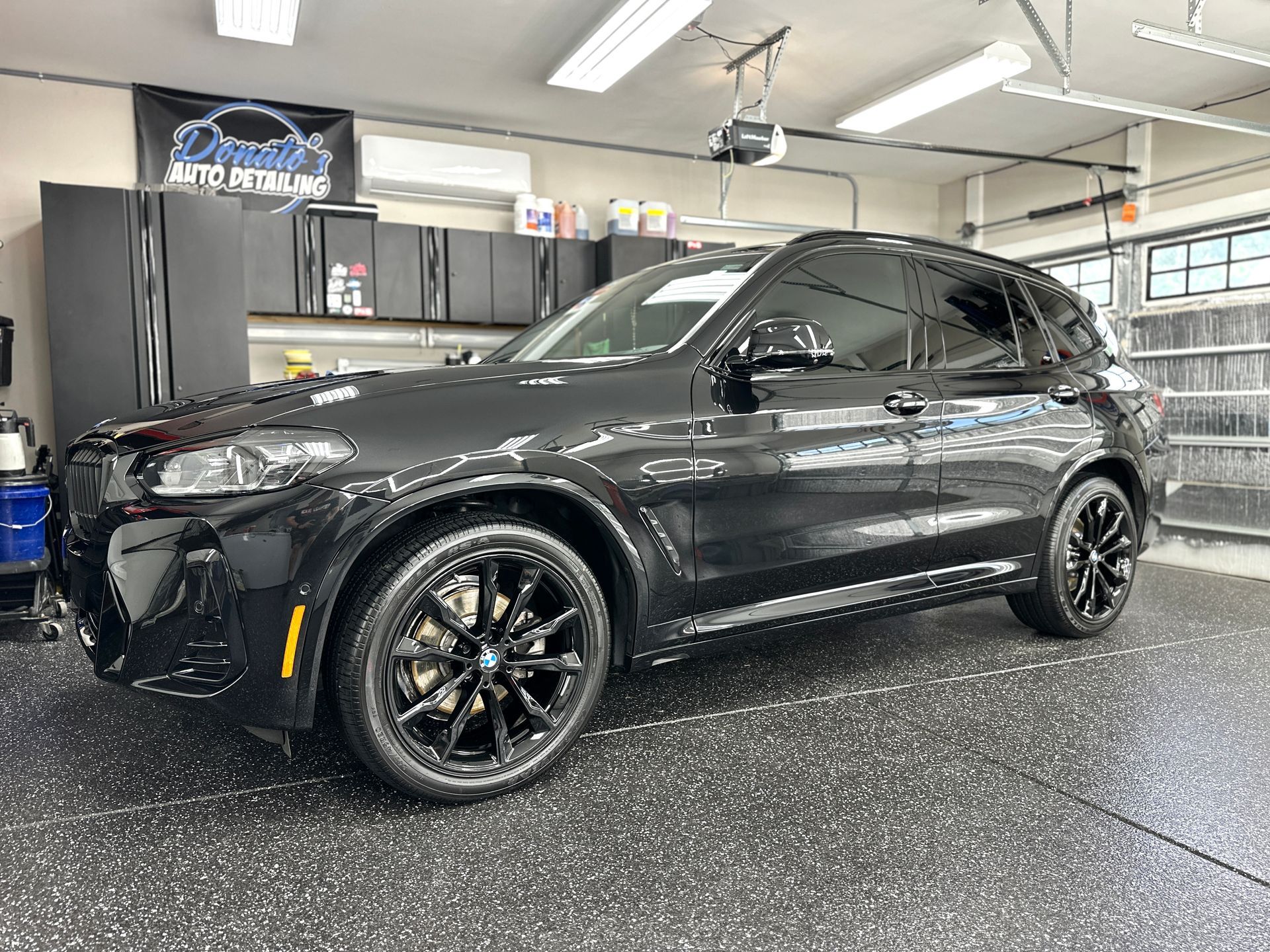 Black BMW X3 SUV in a garage, black wheels, glossy paint.