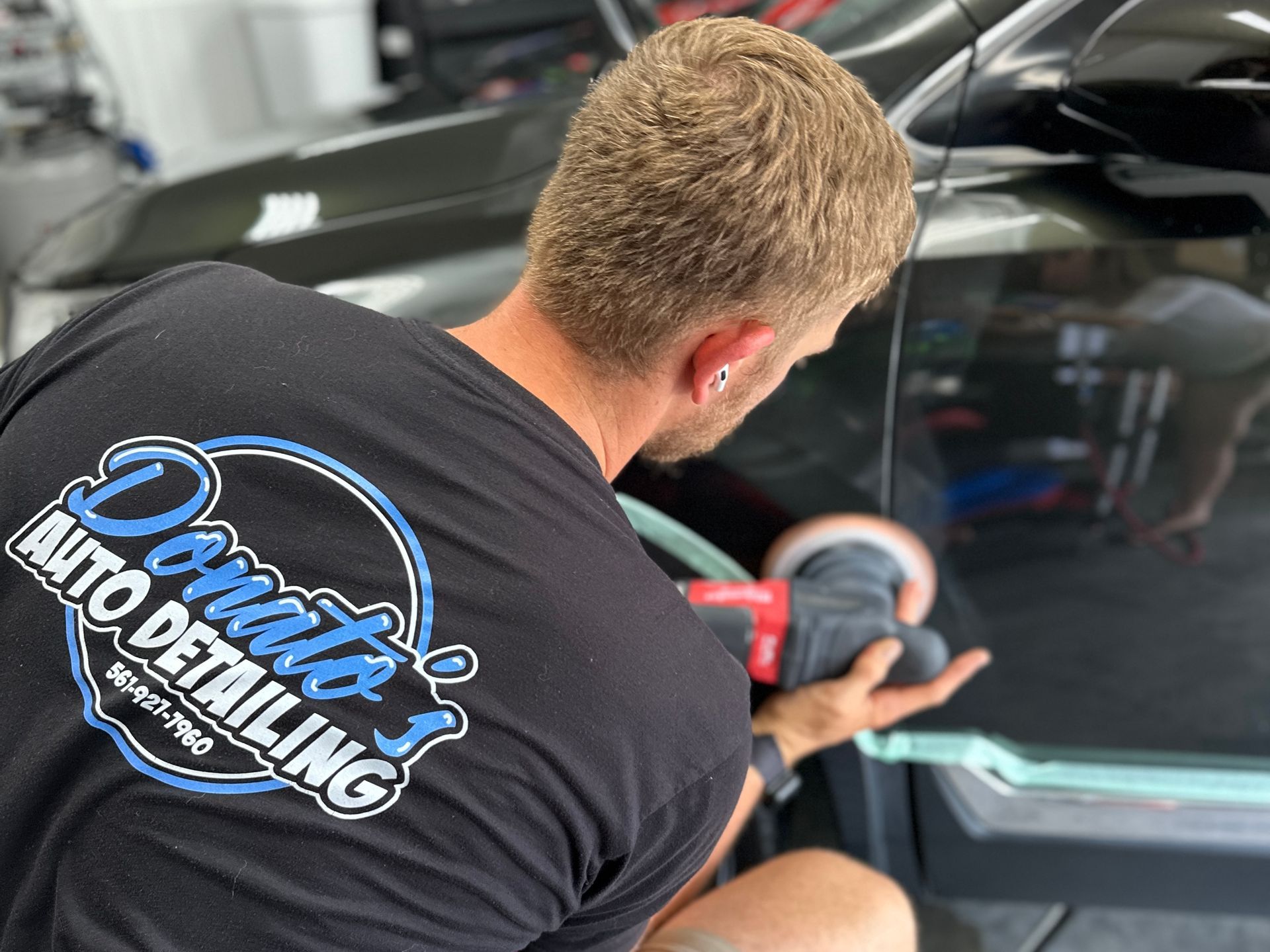 Man polishing a car door with a power buffer, wearing a Donato's Auto Detailing t-shirt.