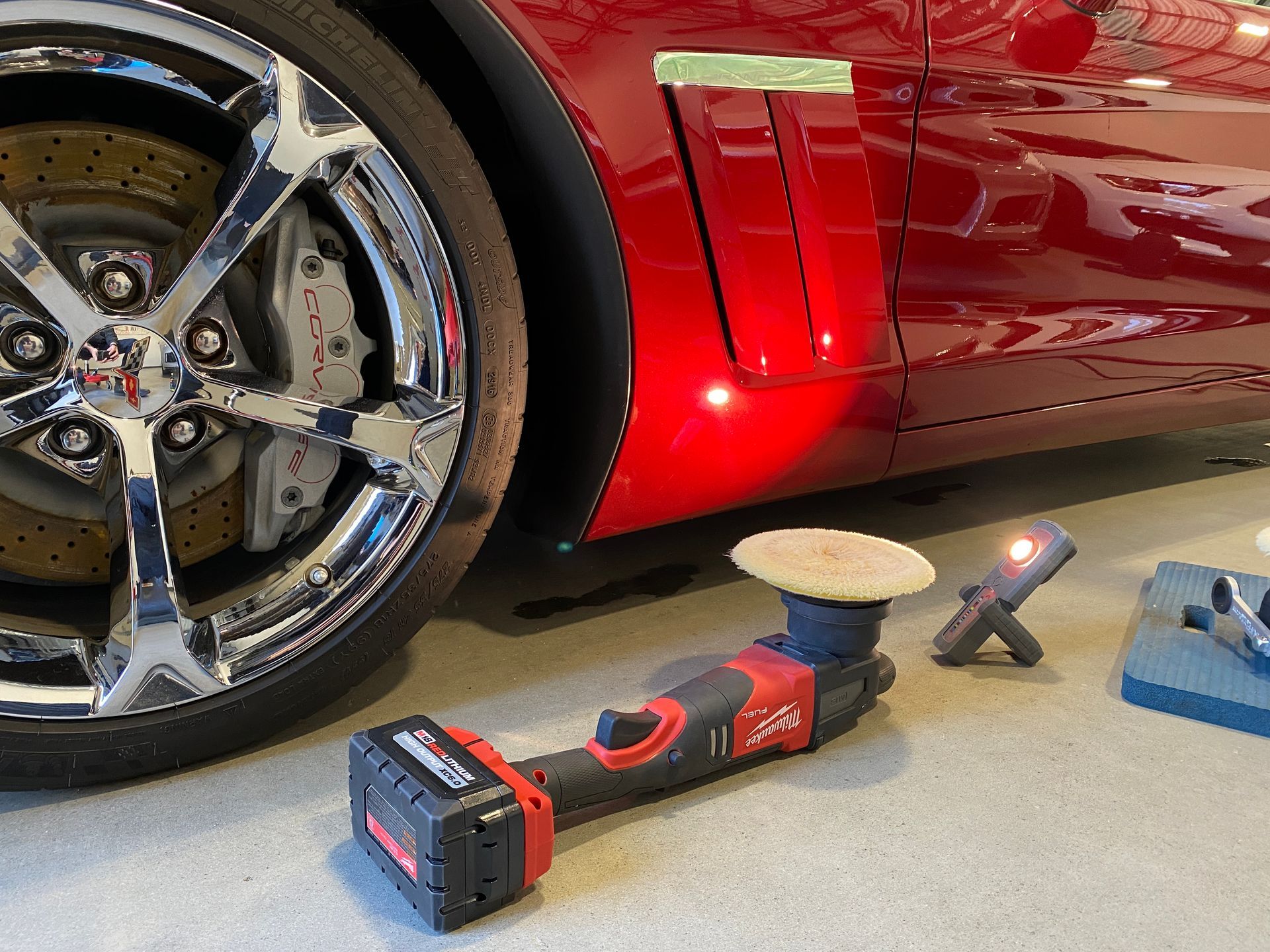 Red sports car being polished, with a buffing tool and wheel.