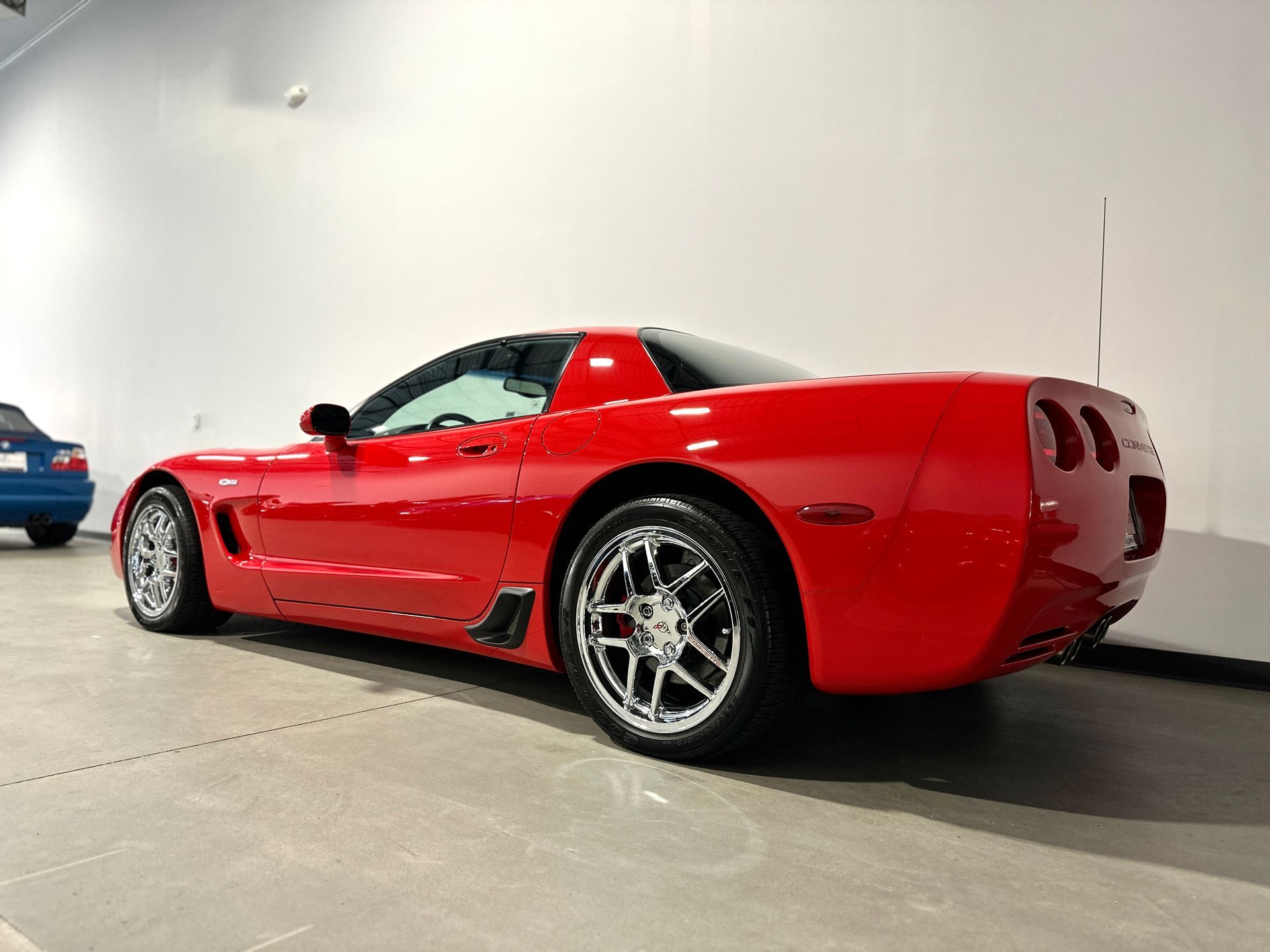 Red Chevrolet Corvette parked indoors, angled rear view. Chrome wheels, black accents, shiny finish.
