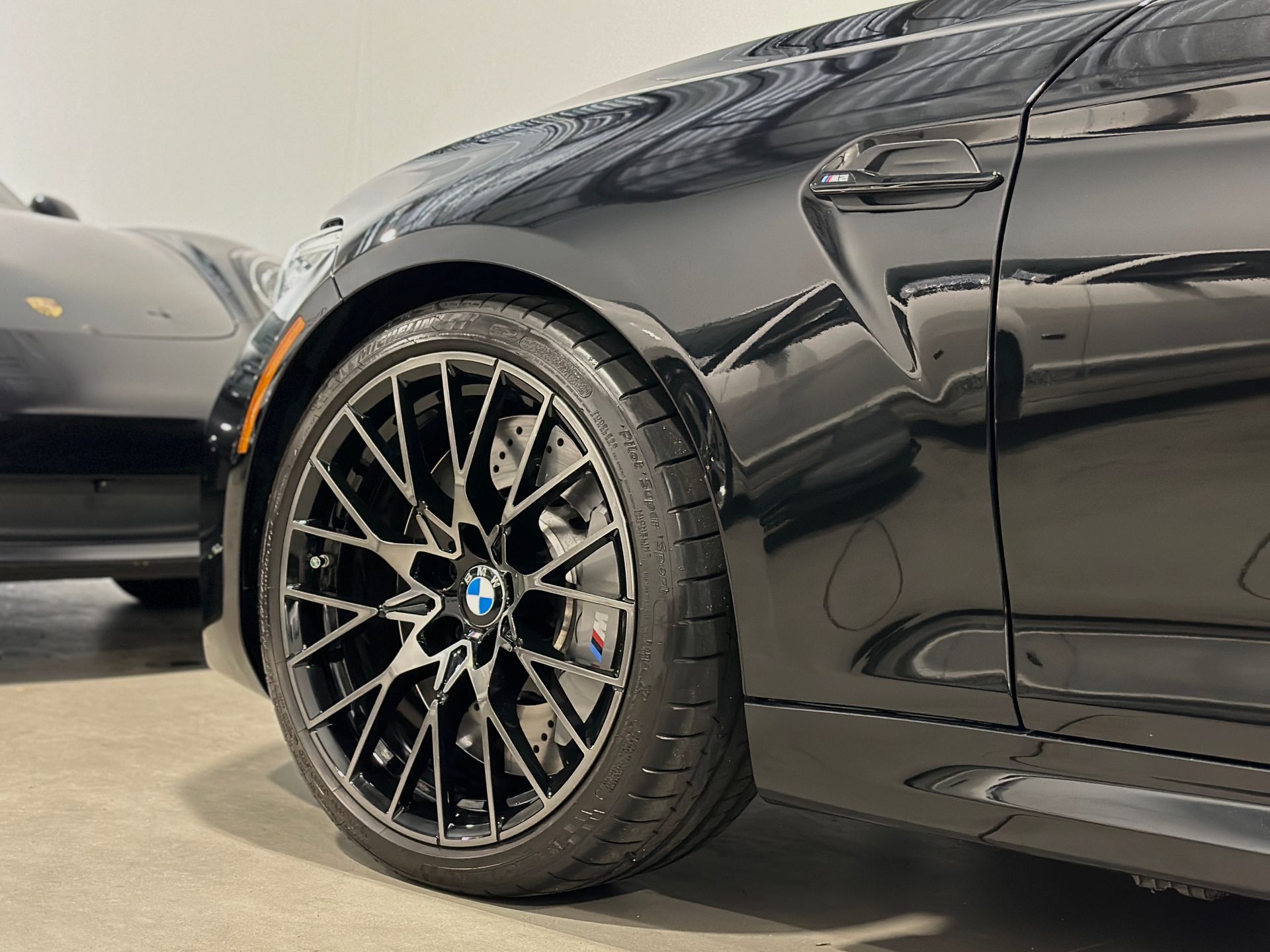 Black BMW car wheel close-up, black rim with blue logo, parked indoors.